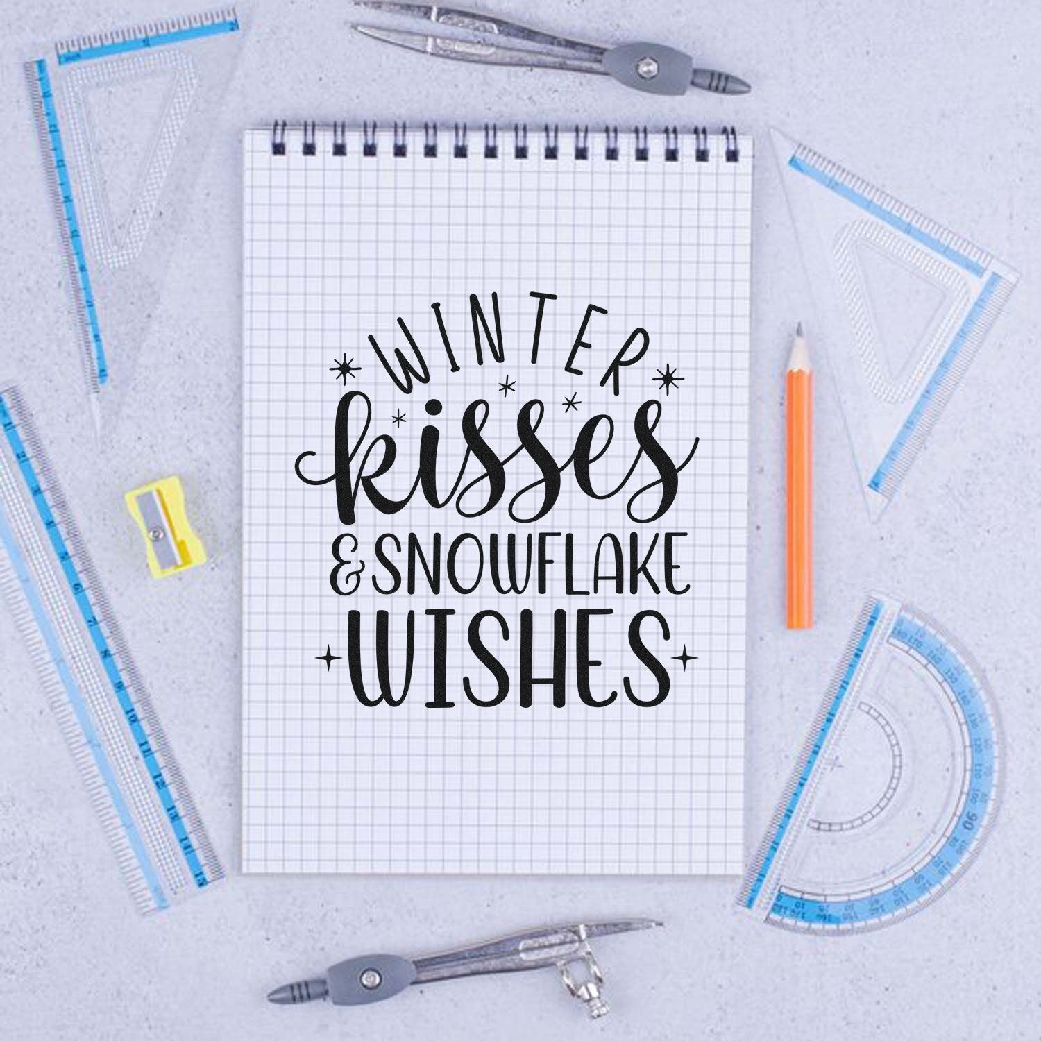 Winter Kisses and Snowflake Wishes rubber stamp design displayed on a sketchpad with drafting tools, ideal for handmade holiday cards.