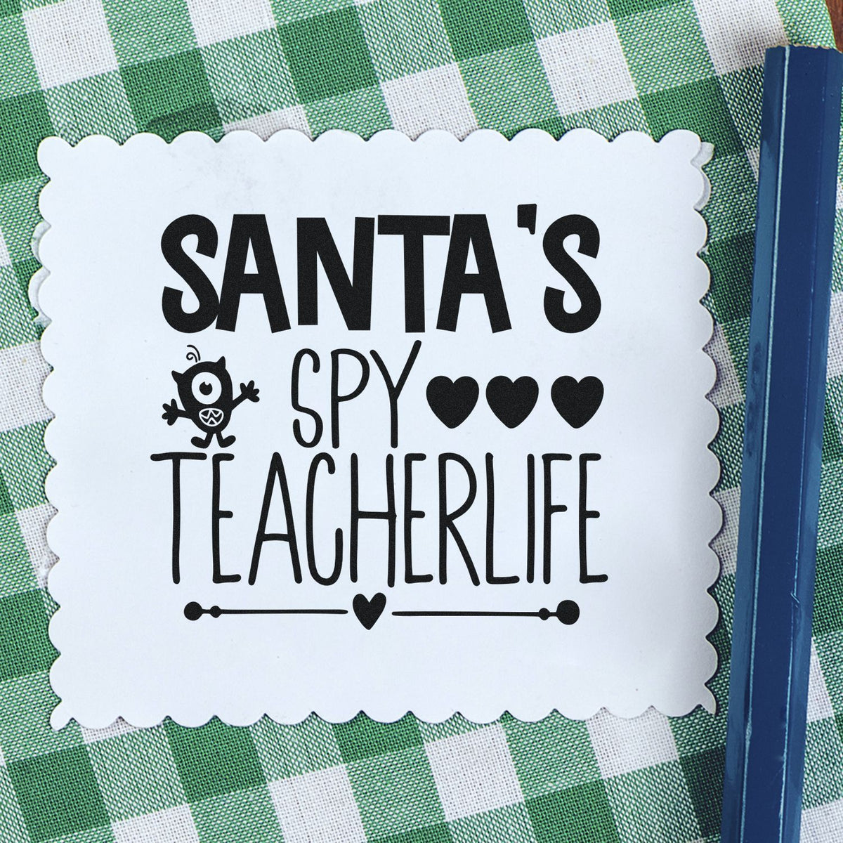 Santa's Spy Teacher Life Premium Wooden Stamp - Vintage Pro imprint stamped in black ink. The words "Santa's spy teacherlife" include a small Santa face, hearts, and an underline.