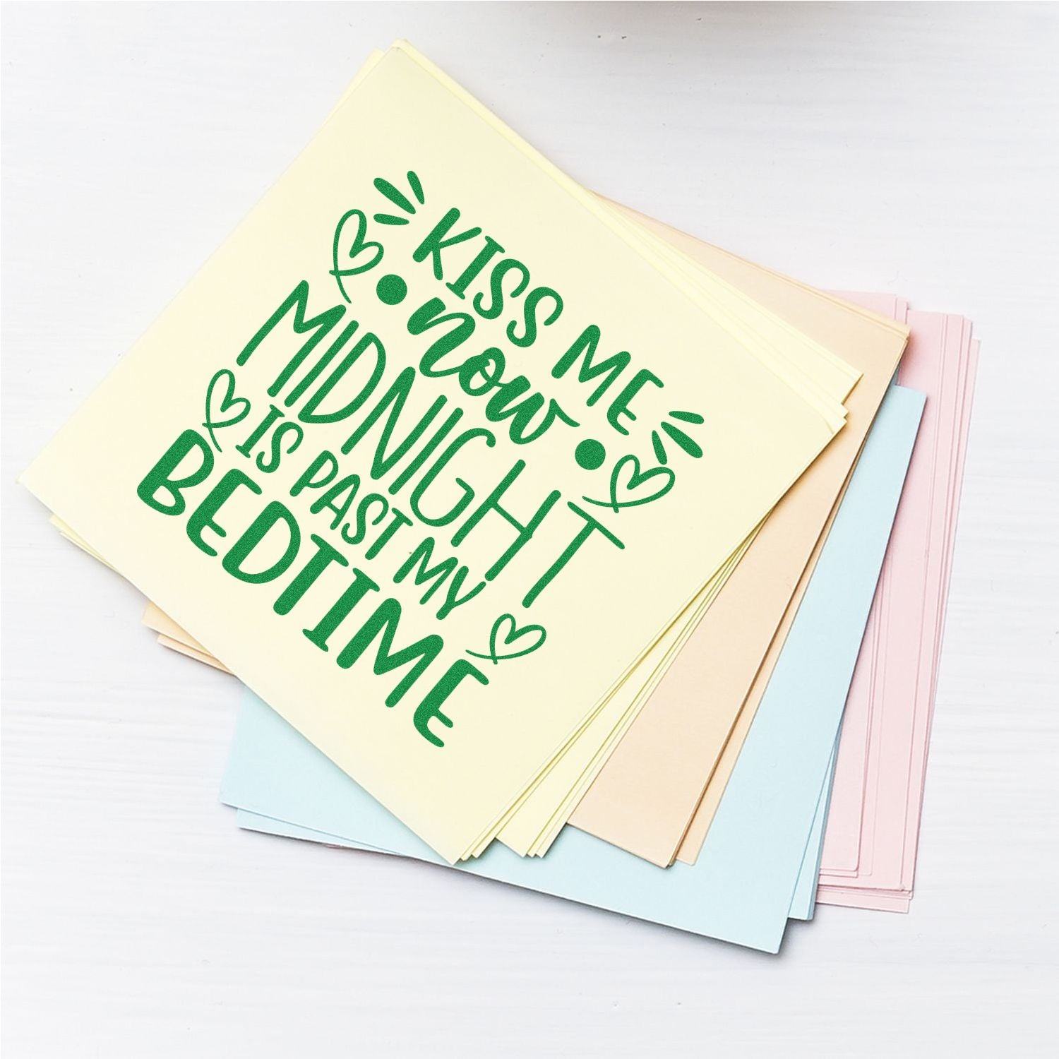 Funny rubber stamp design reading Kiss me now, midnight is past my bedtime on a stack of pastel paper sheets.