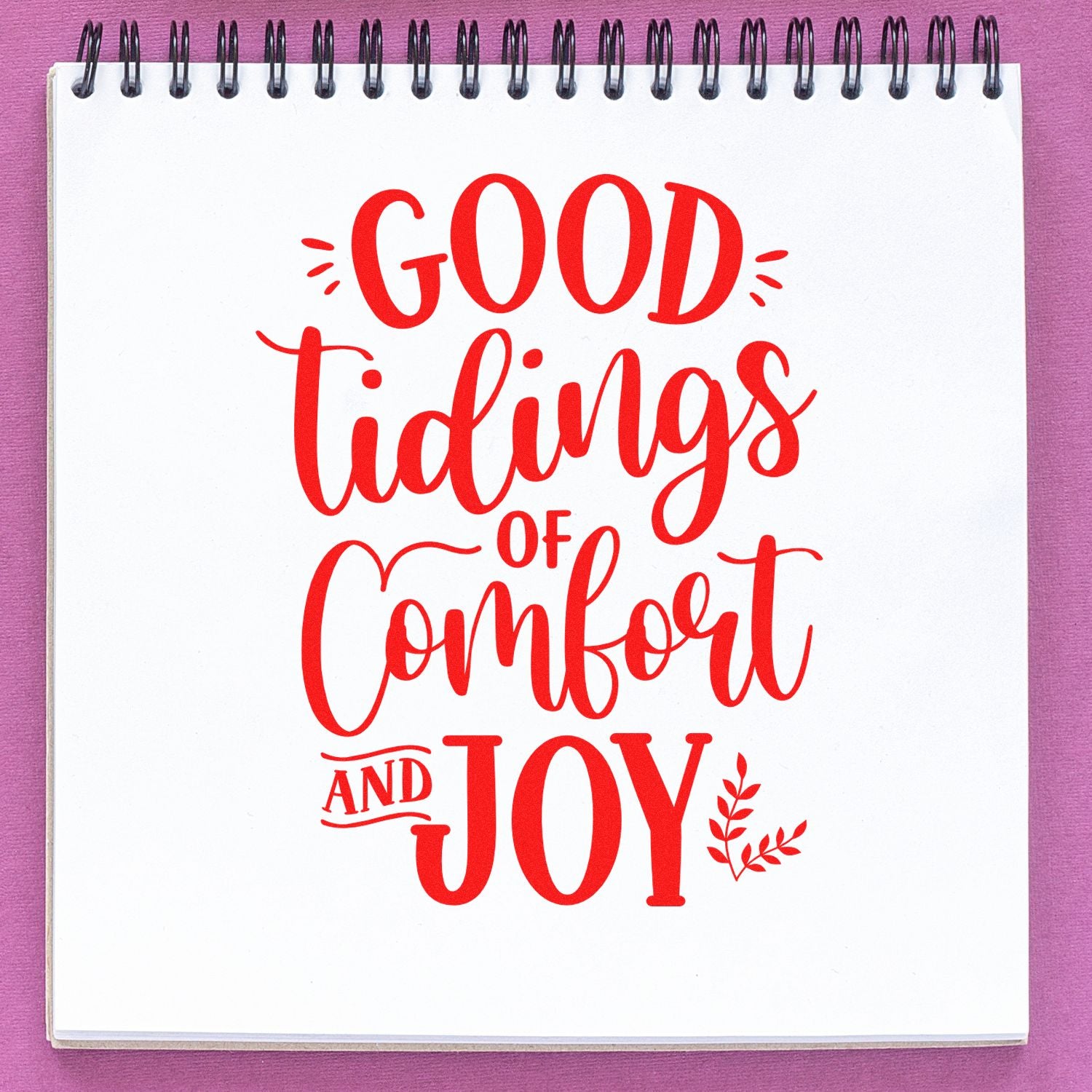 Christmas rubber stamp design with red Good Tidings of Comfort and Joy lettering on a notebook page.