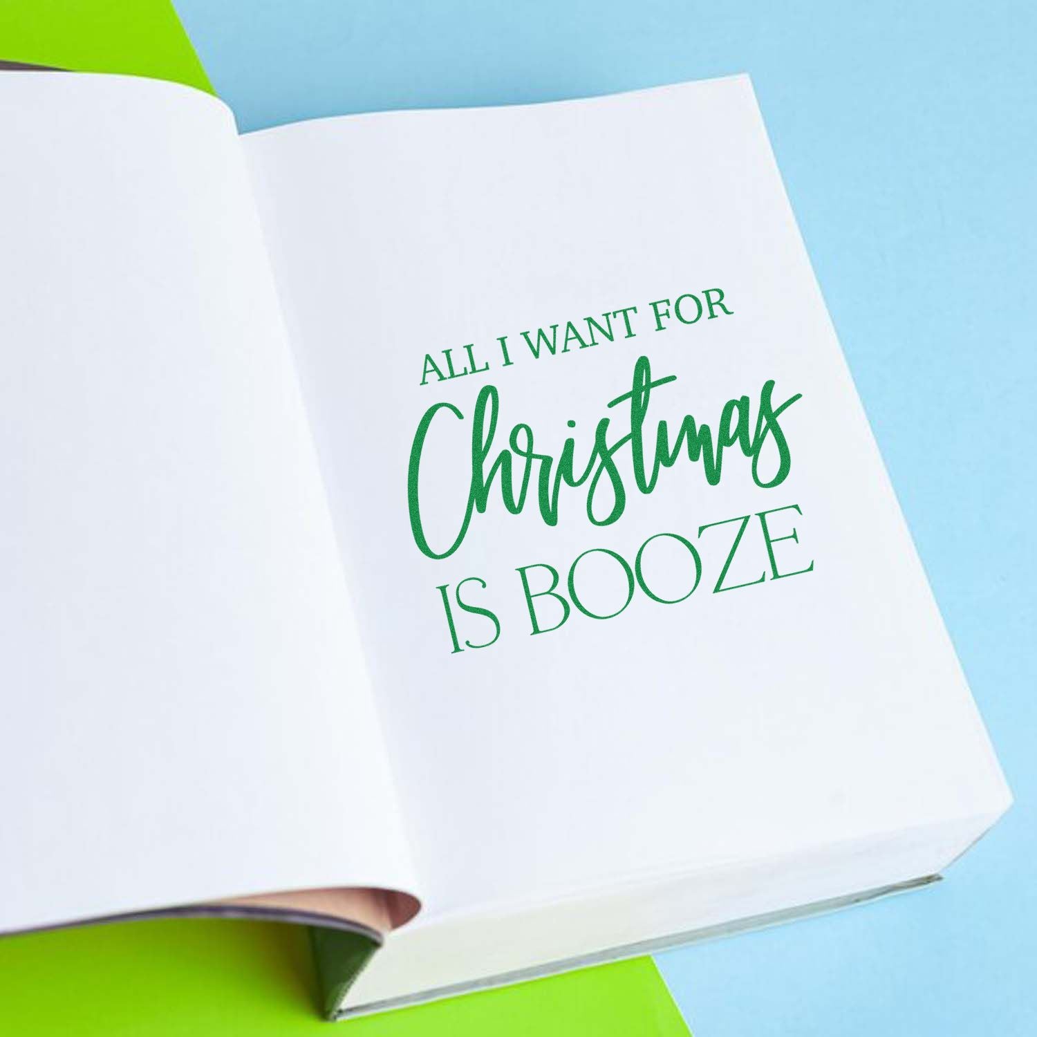 Christmas rubber stamp design reading All I want for Christmas is booze in green on an open notebook page.