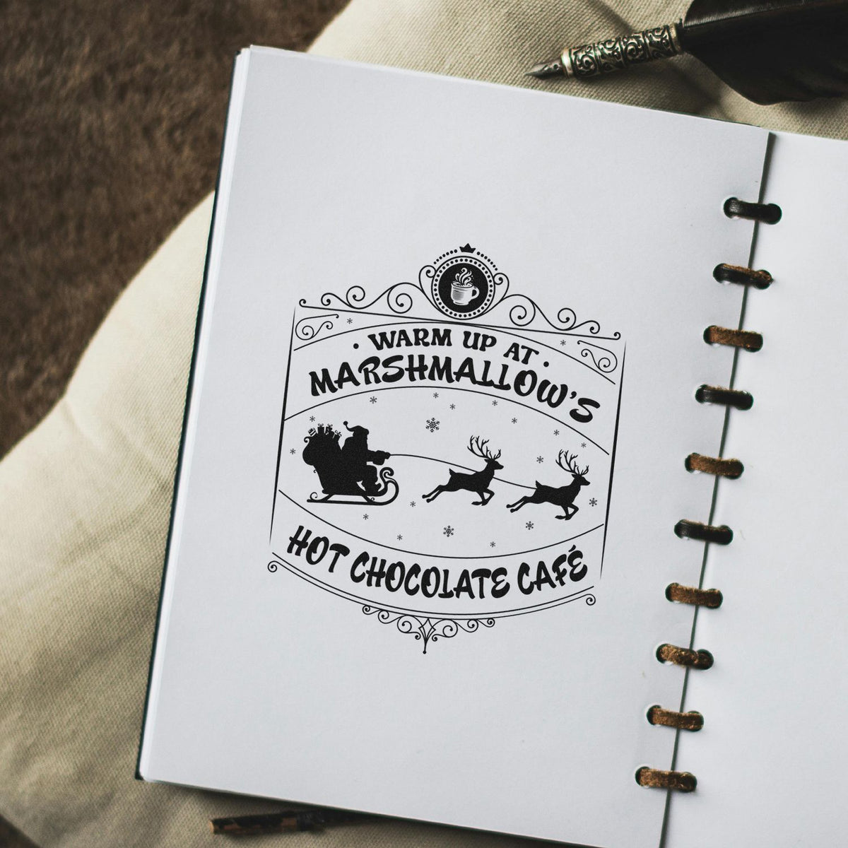 Warm Up At Marshmallow's Hot Chocolate Cafe Premium Wooden Stamp - Vintage Pro imprint stamped in black ink. An ornate vintage sign reads "Warm up at Marshmallow's Hot Chocolate Cafe" with Santa's sleigh and flying reindeer.