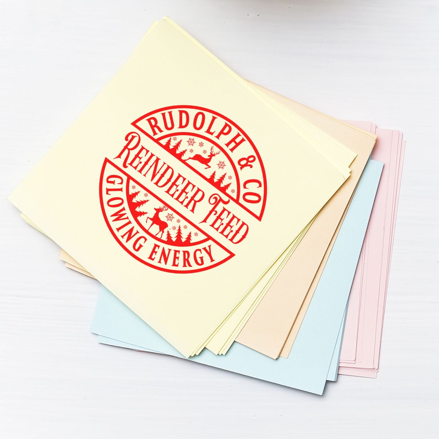 Custom holiday rubber stamp on pastel paper stack reading Rudolph & Co Reindeer Feed, ideal for festive packaging and crafts