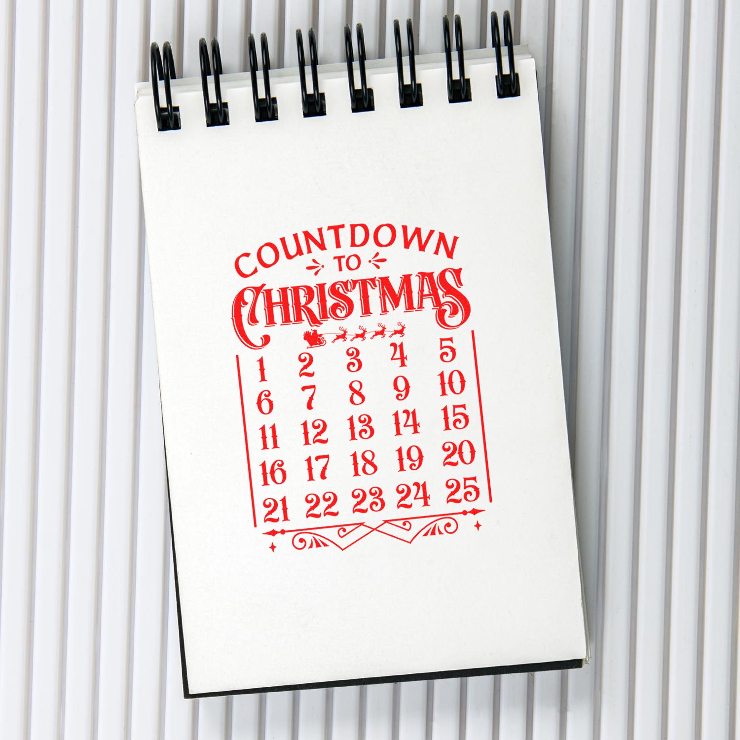 Countdown to Christmas rubber stamp design on a spiral notepad, featuring a red holiday calendar from 1 to 25.