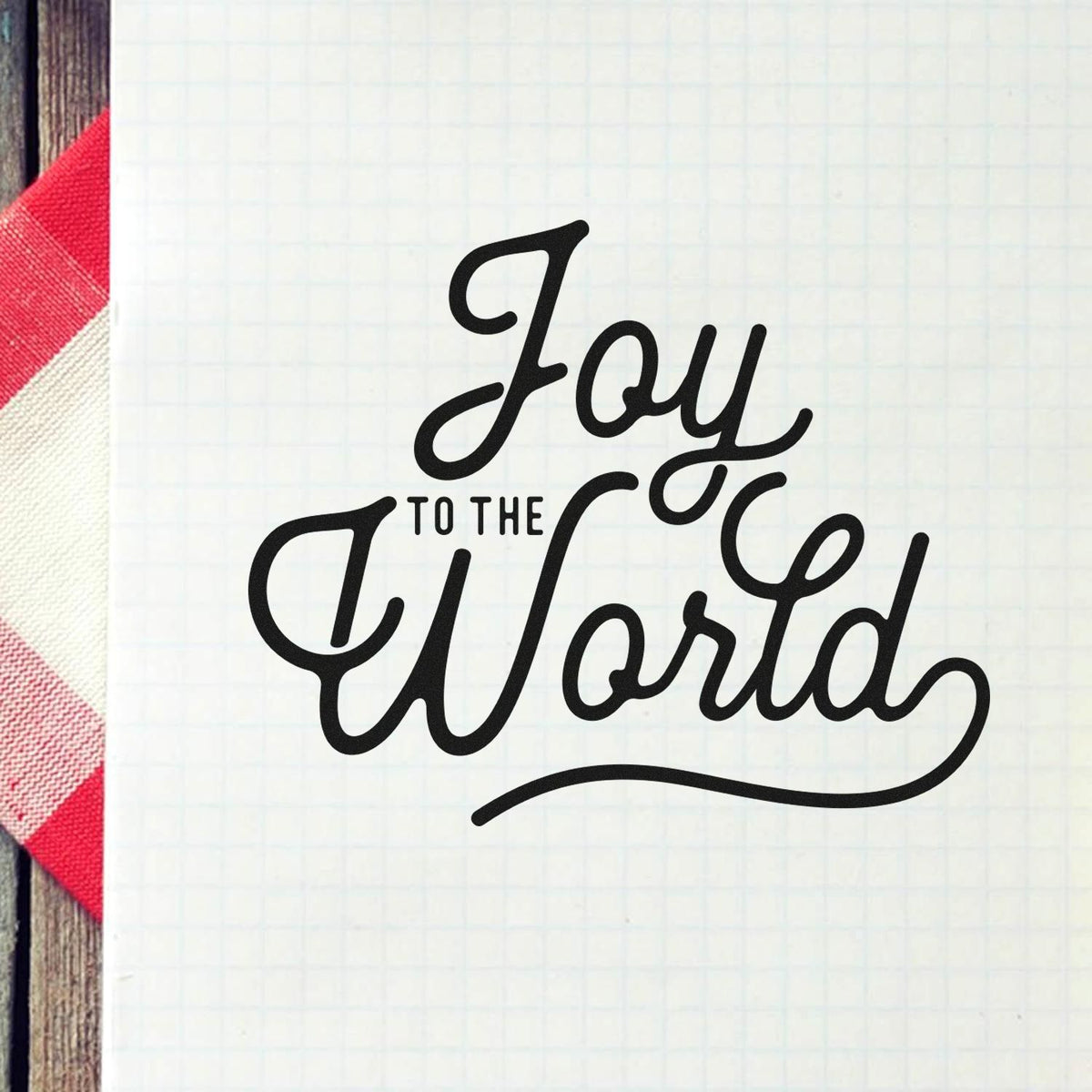 Premium Wooden Joy To The World Script Lettering Stamp - Vintage Pro imprint stamped in black ink. The words "Joy to the world" combine oversized cursive with small connecting text.
