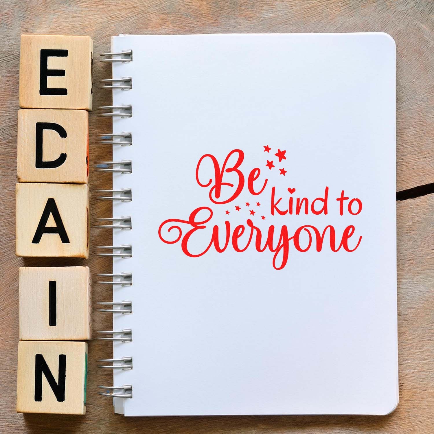 Wooden alphabet rubber stamps beside a notebook with Be kind to Everyone lettering, showcasing custom craft stamp design.
