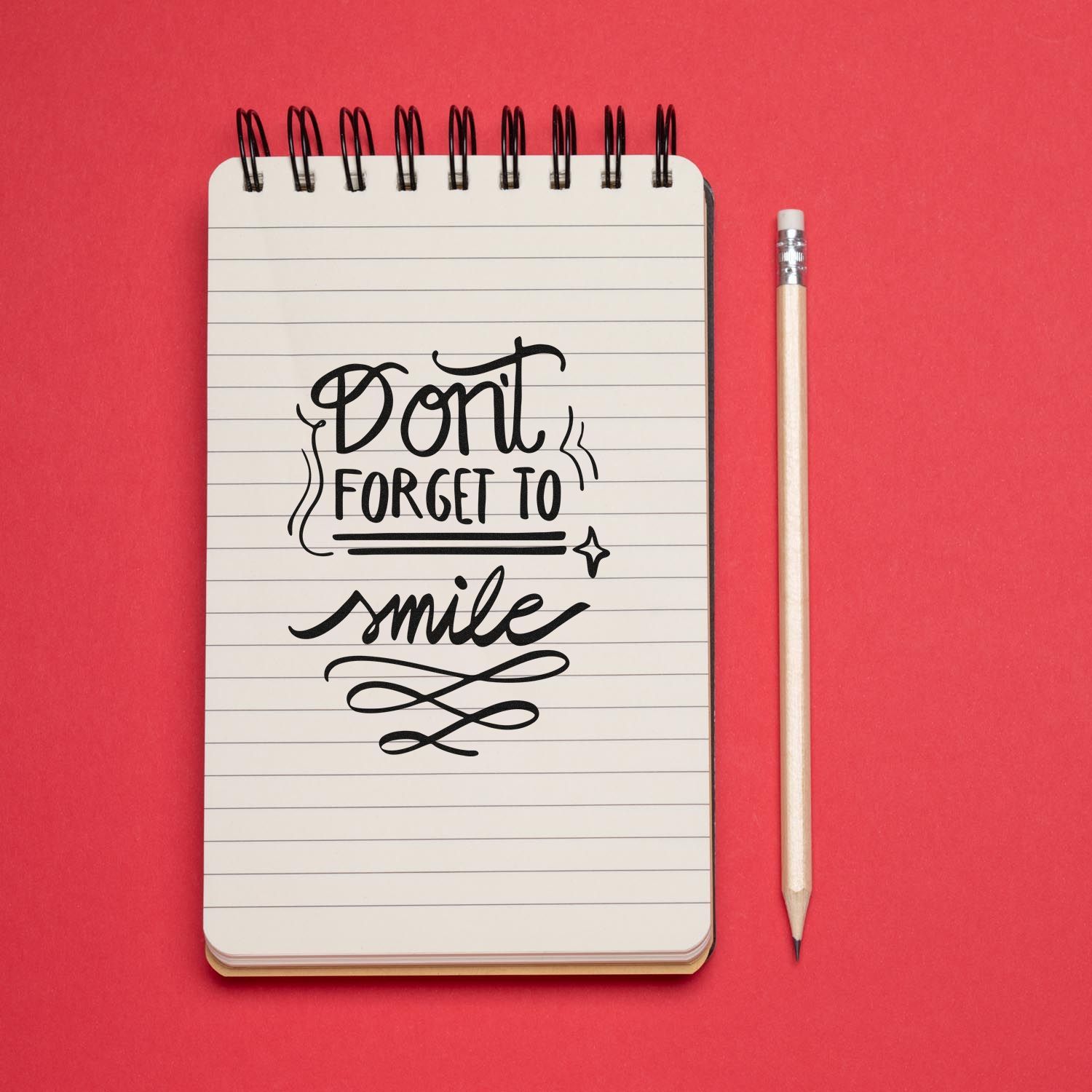 Dont Forget to Smile decorative rubber stamp design on a lined notebook with pencil on a red background