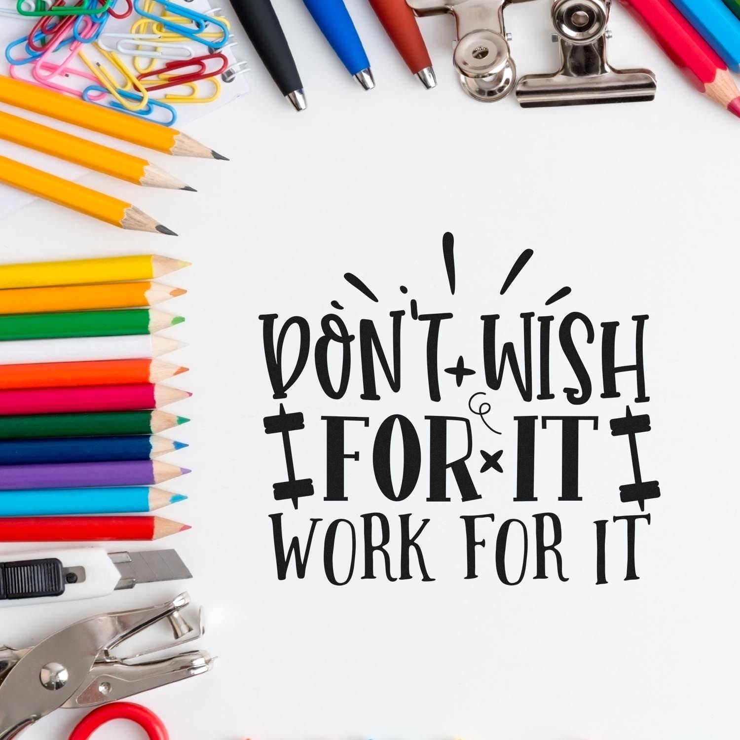 Motivational rubber stamp design reading Dont Wish for It, Work for It surrounded by pencils, pens, and office supplies.