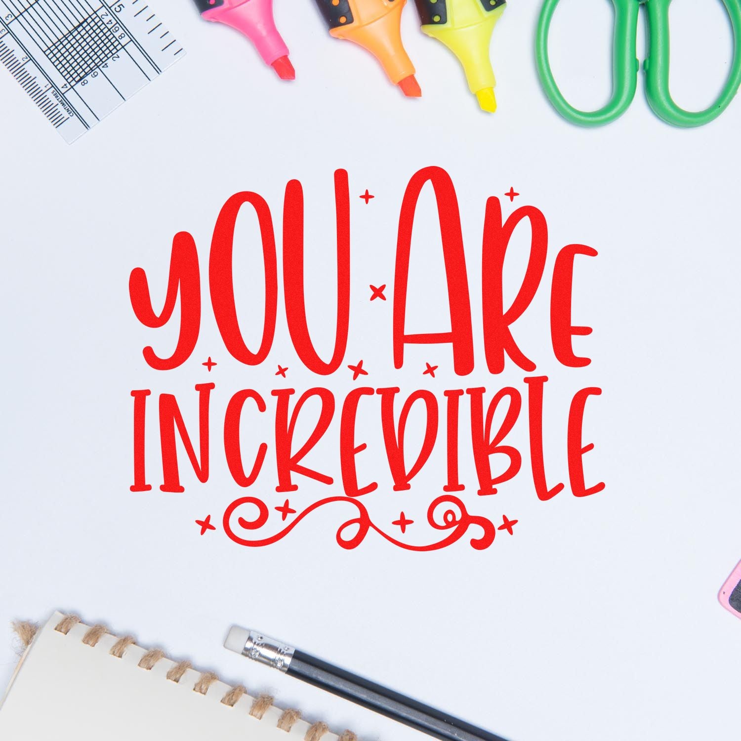 Motivational rubber stamp design with red You Are Incredible lettering and stationery supplies on white background.