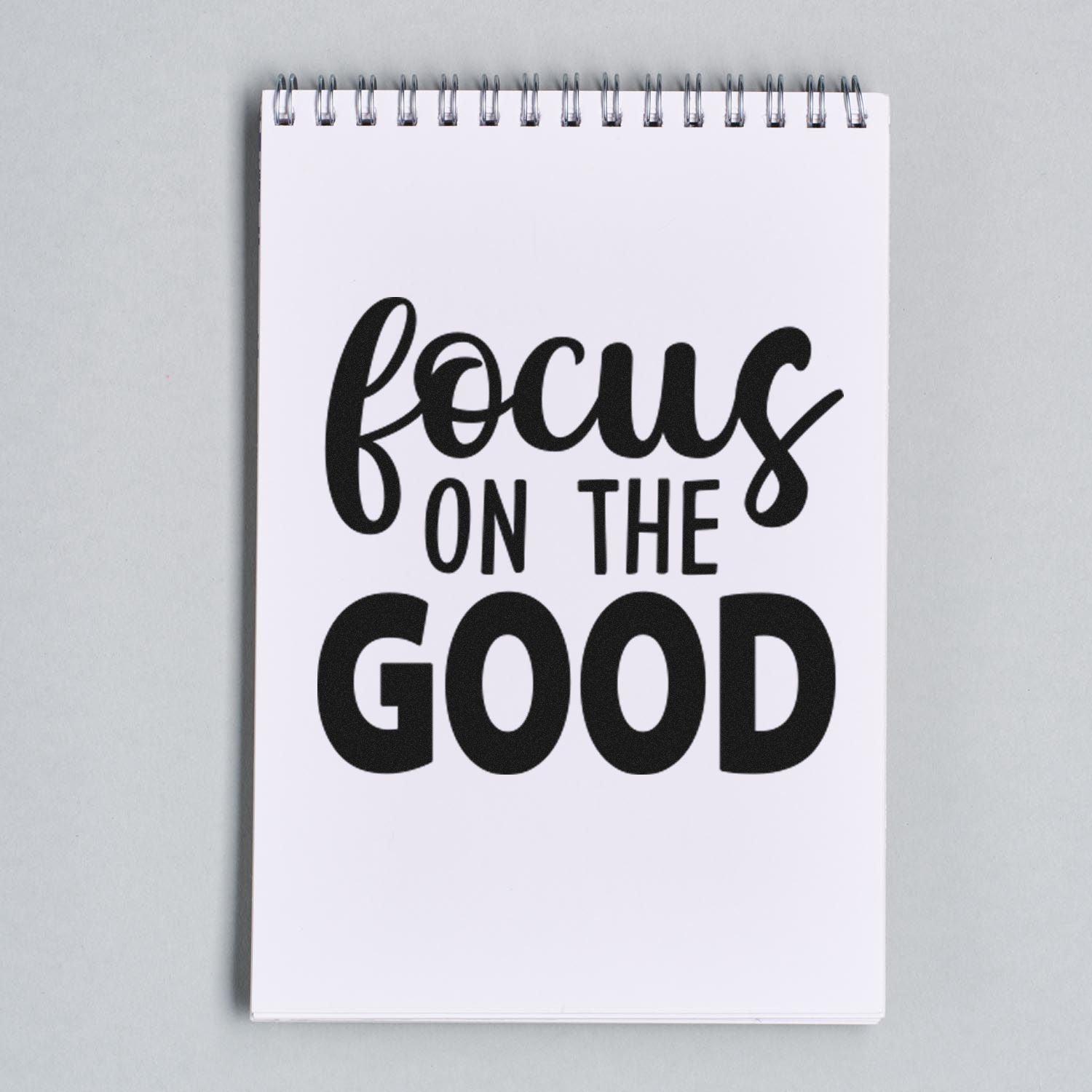 Custom rubber stamp design featuring Focus on the Good in bold black lettering on a white spiral notebook.