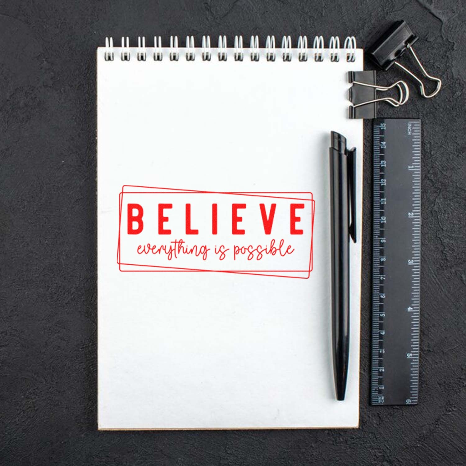 Motivational rubber stamp design with red BELIEVE everything is possible imprint on a notebook, ideal for crafts and branding.