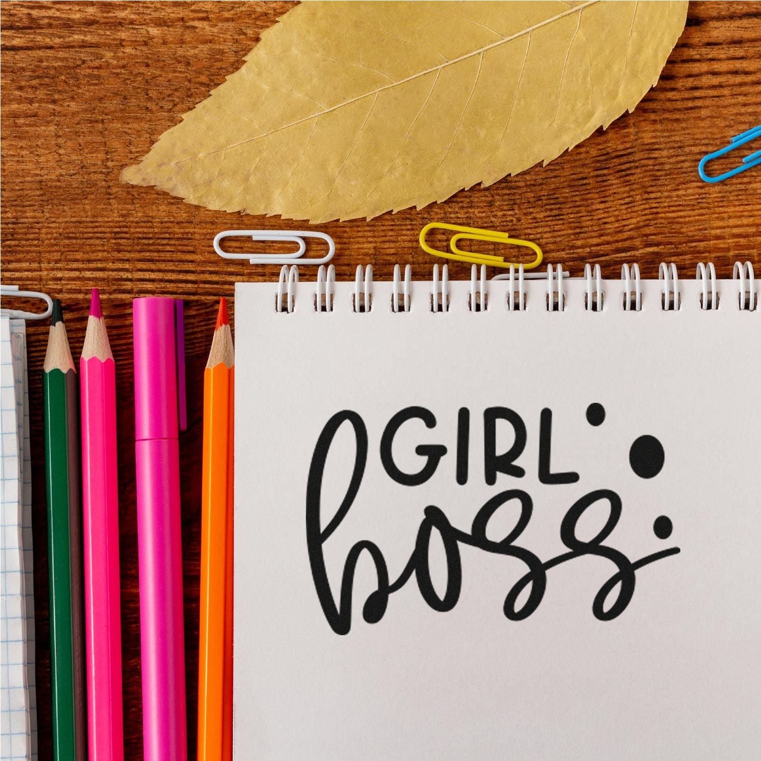 Girl Boss rubber stamp on notebook with colorful pencils and paper clips, ideal for planners and DIY craft projects.