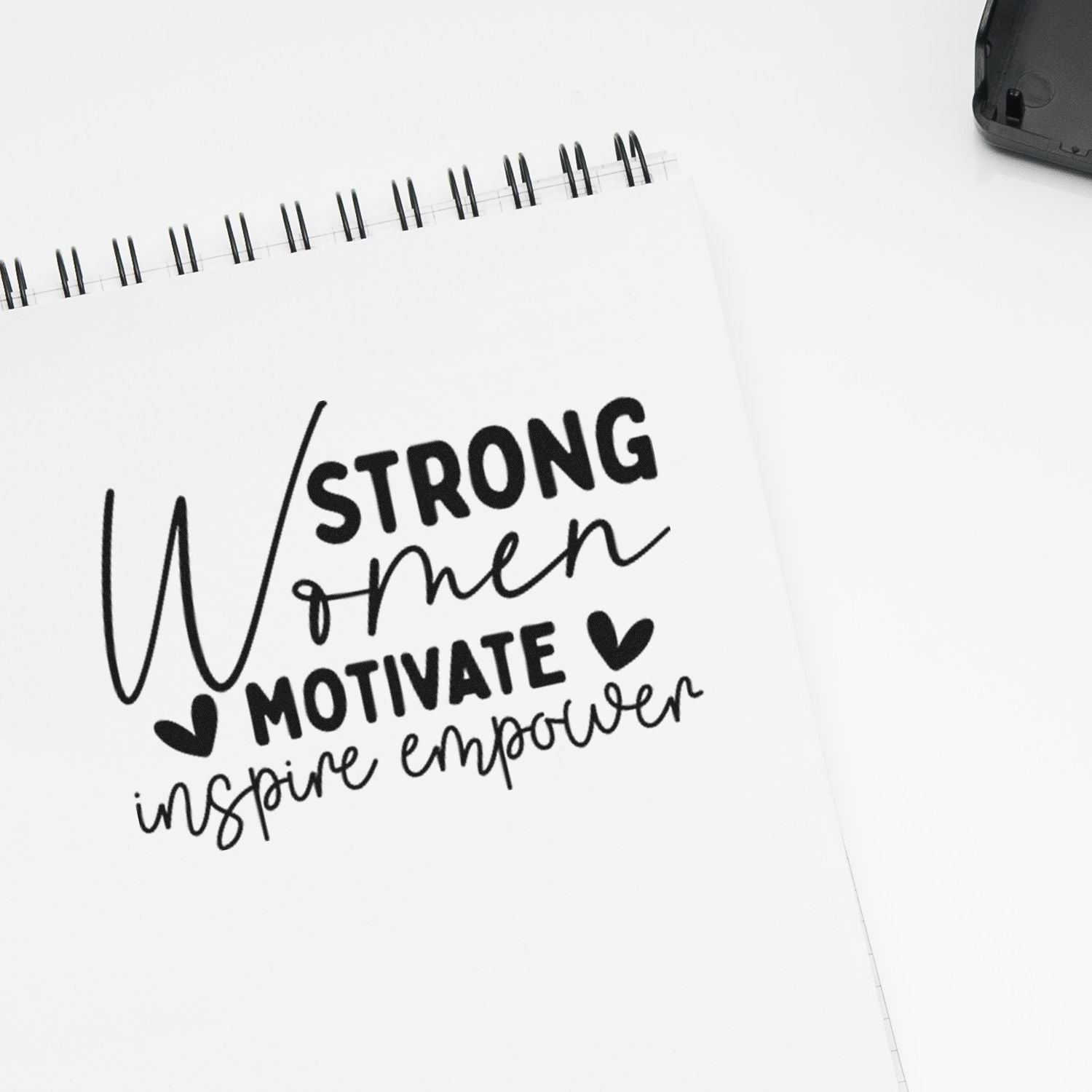 Strong Women Motivate, Inspire, Empower rubber stamp design on a white notebook page.