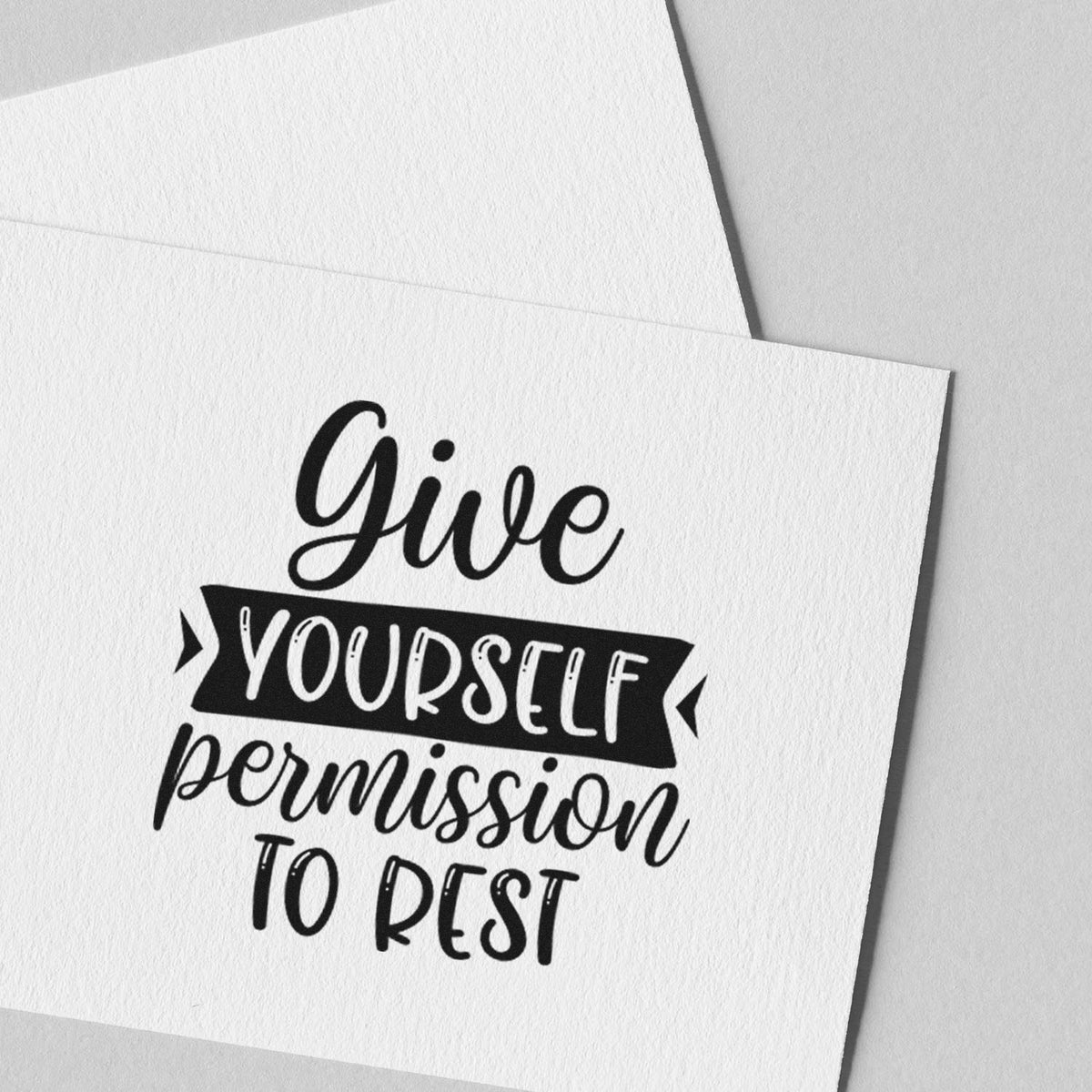 Vintage Pro Give Yourself Permission To Rest Premium Wooden Stamp imprint stamped in black ink. The phrase "Give yourself permission to rest" includes a dark ribbon banner around "yourself."