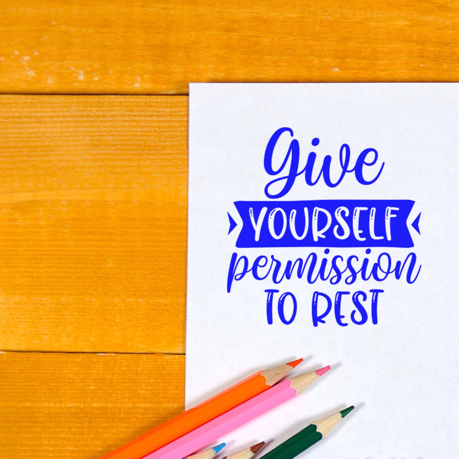 Self-care rubber stamp design reading Give yourself permission to rest on white paper with colored pencils.