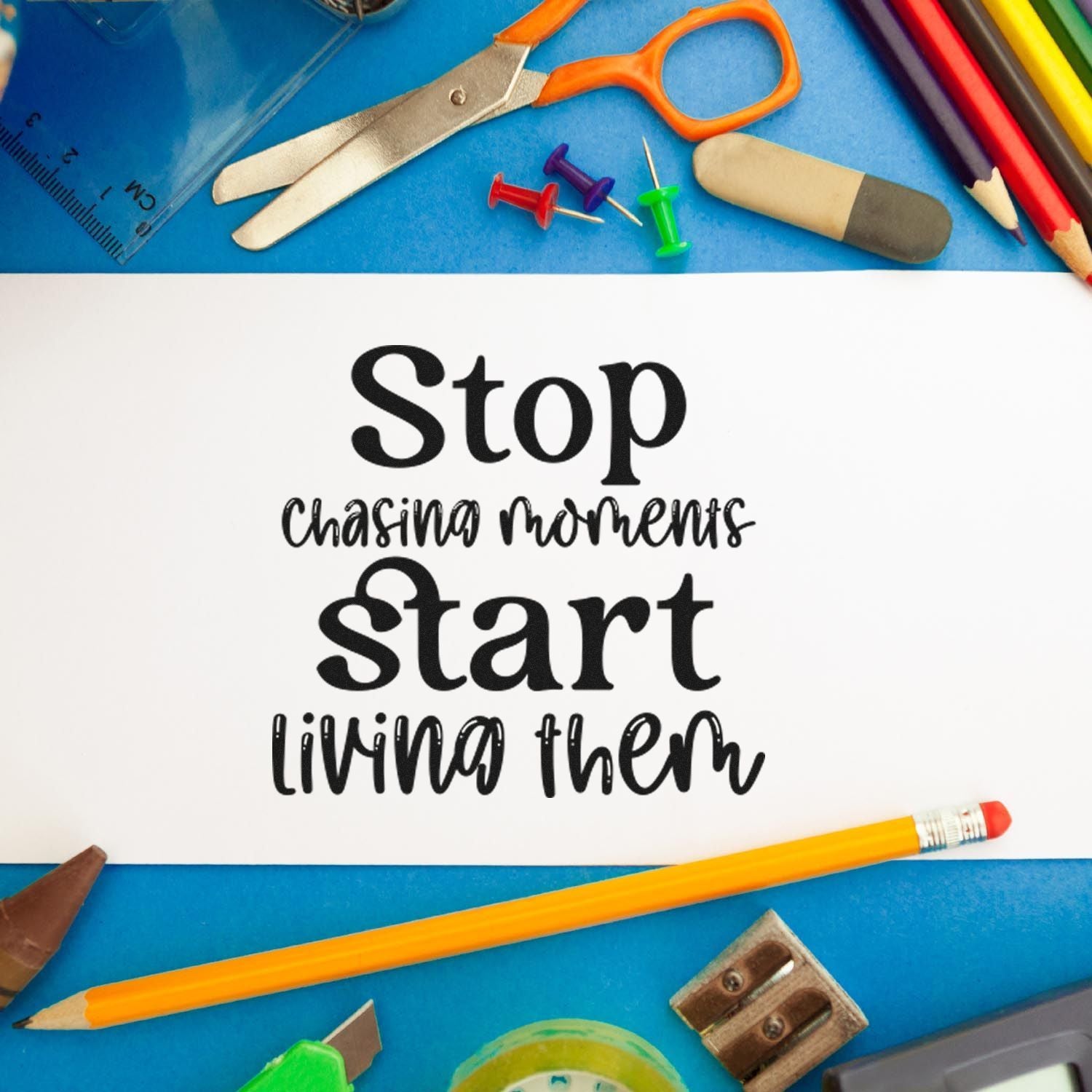 Inspirational rubber stamp quote reading Stop chasing moments, start living them on white paper with school supplies.