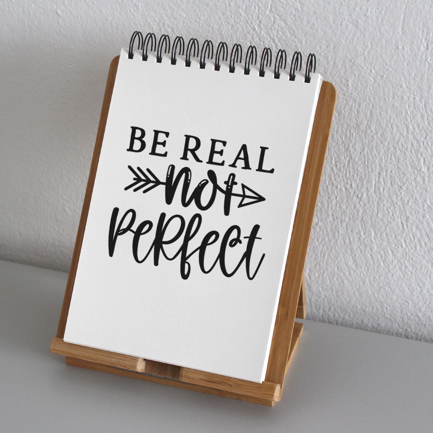 Be Real Not Perfect rubber stamp design displayed on a spiral notebook in a wooden stand, ideal for motivational craft projects.