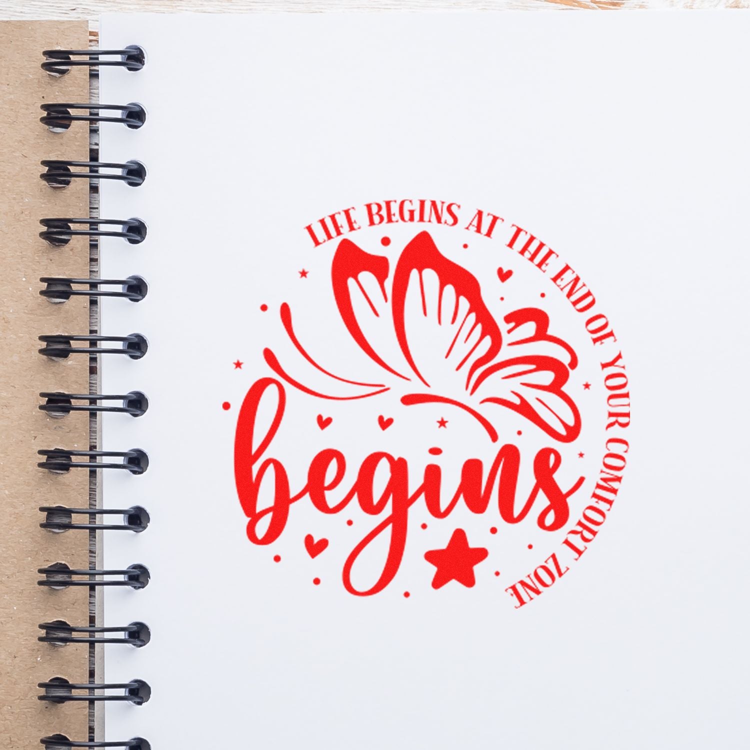 Red butterfly motivational rubber stamp reading Life Begins at the End of Your Comfort Zone on a spiral notebook page.