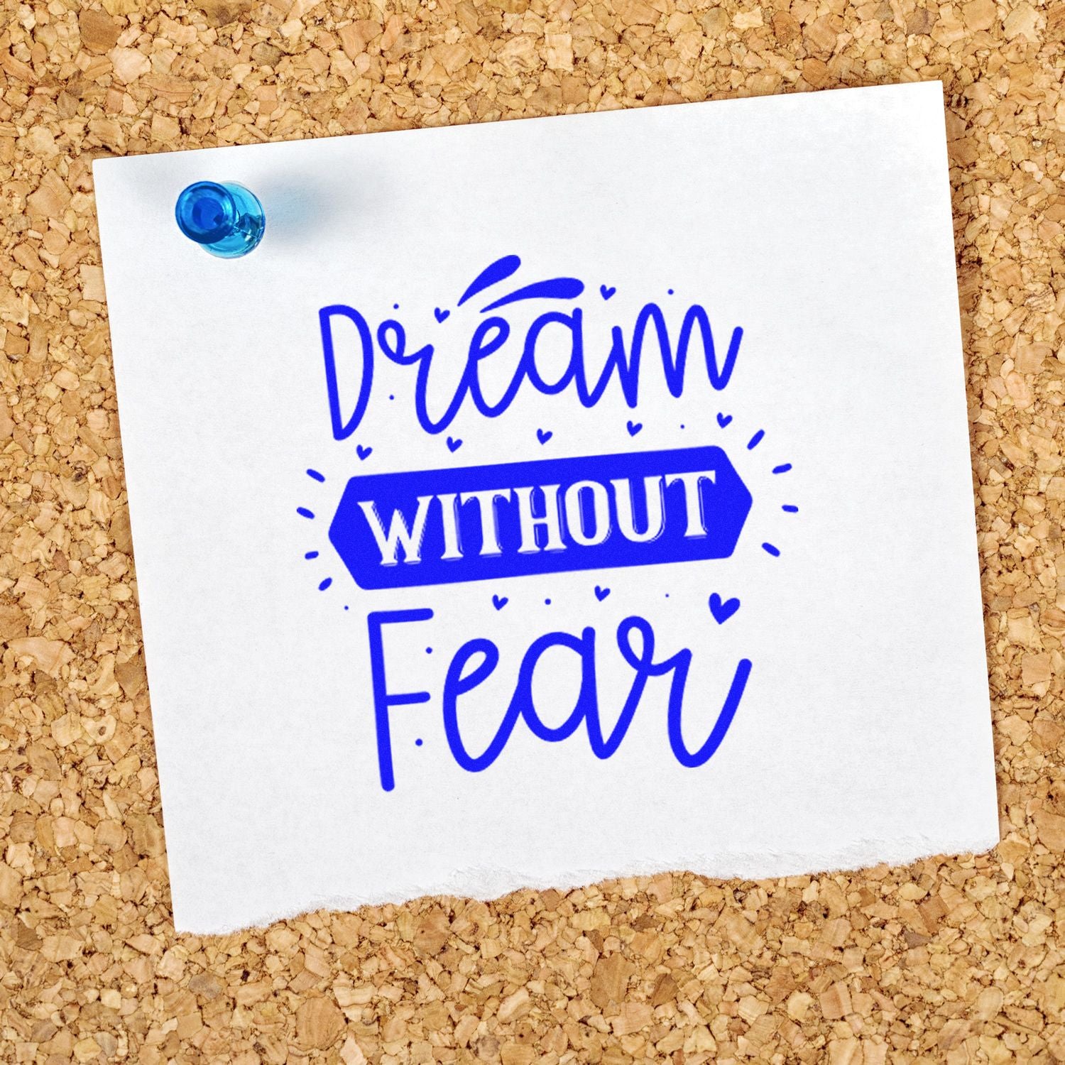 Blue inspirational rubber stamp with Dream Without Fear message on white paper pinned to a corkboard.