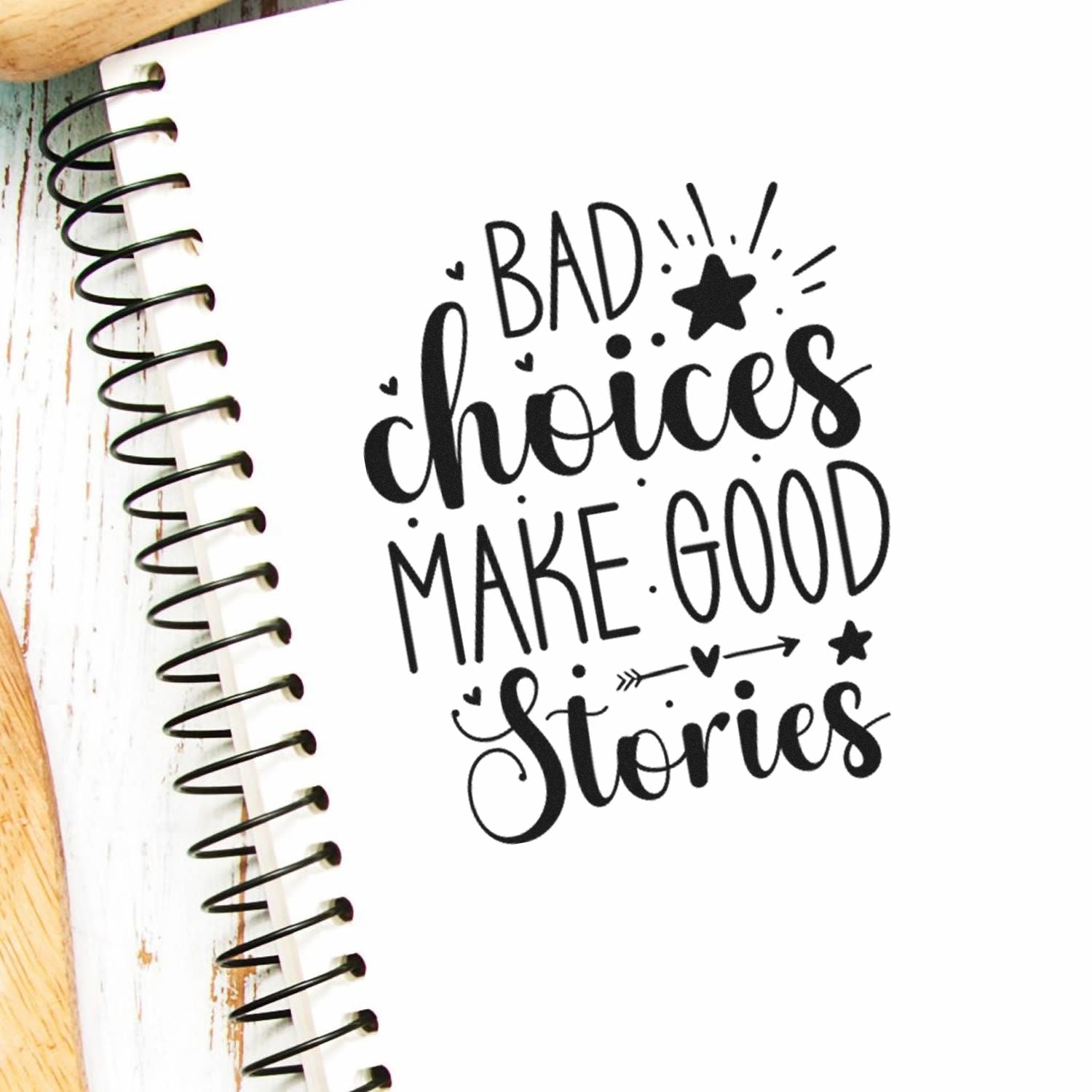 Funny rubber stamp design reading Bad choices make good stories stamped on a spiral notebook page.