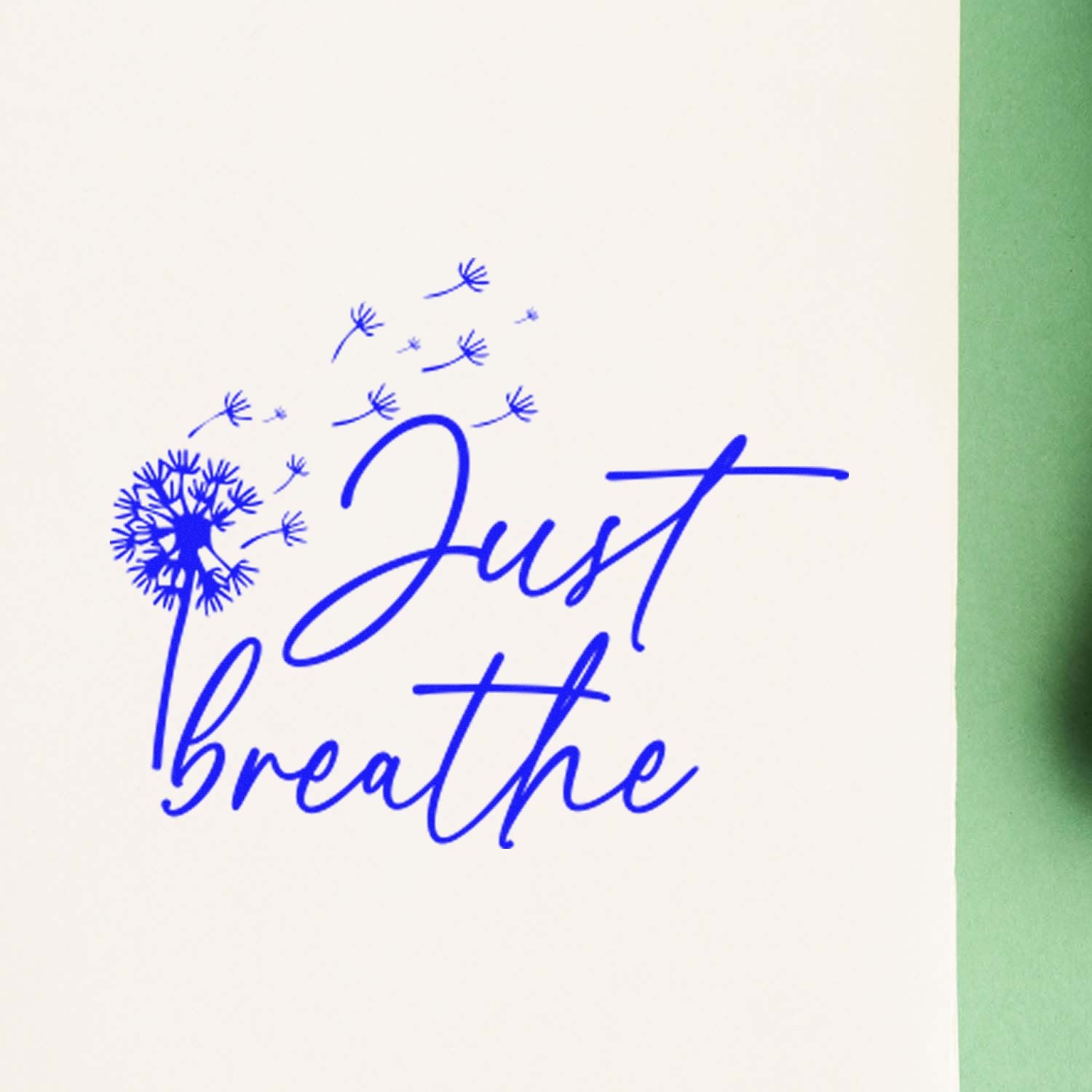 Inspirational rubber stamp reading Just Breathe with dandelion design in blue ink on white paper.