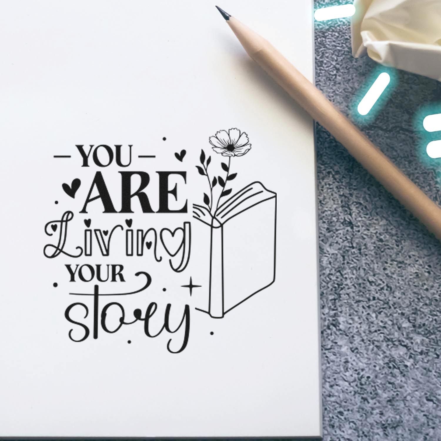 Inspirational rubber stamp design reading You Are Living Your Story with open book and flower illustration.