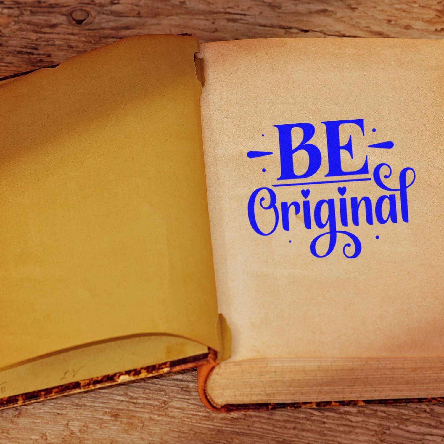 Blue Be Original rubber stamp impression on an open vintage book, ideal for custom stationery and craft branding.