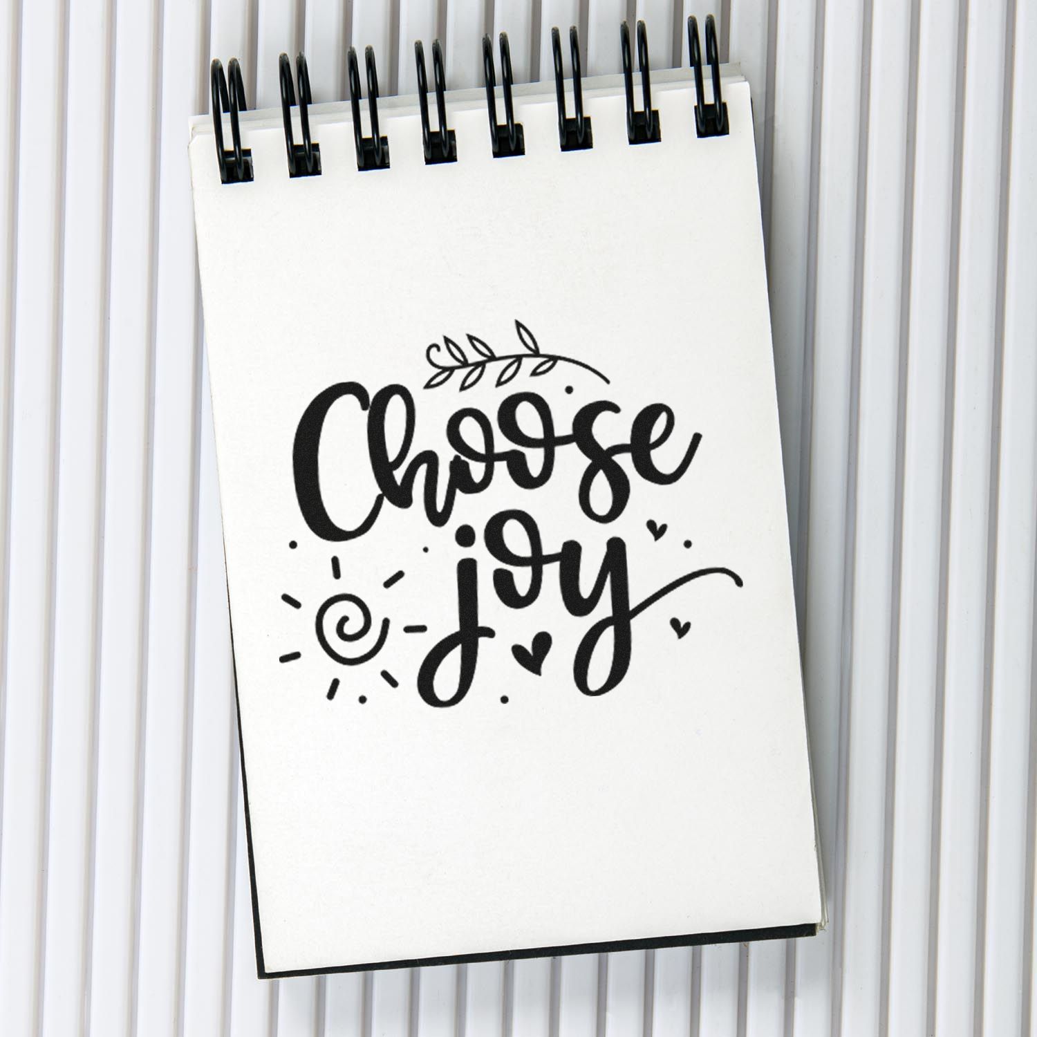 Choose Joy hand-lettered custom rubber stamp design on a spiral notebook with floral and heart doodles for crafting.