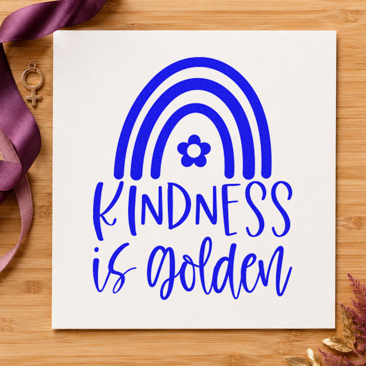 Kindness Golden Flower Rainbow craft stamp imprinted in blue ink on paper, a design suited to framed playground fence.