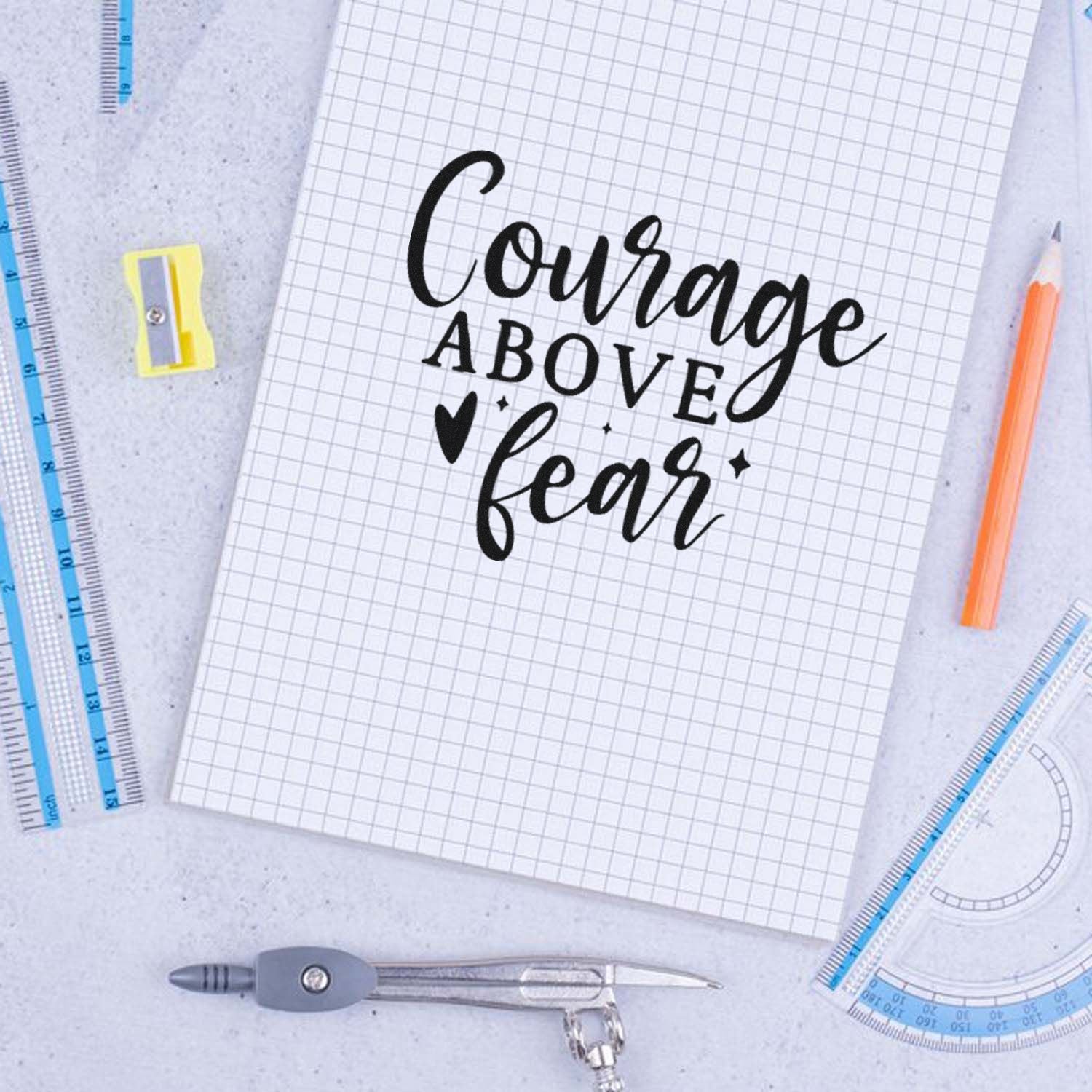 Courage Above Fear rubber stamp design on graph paper, surrounded by school supplies and drafting tools.