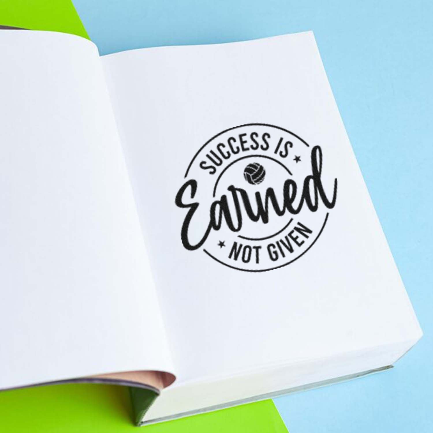 Motivational rubber stamp imprint reading Success Is Earned Not Given on a notebook page.