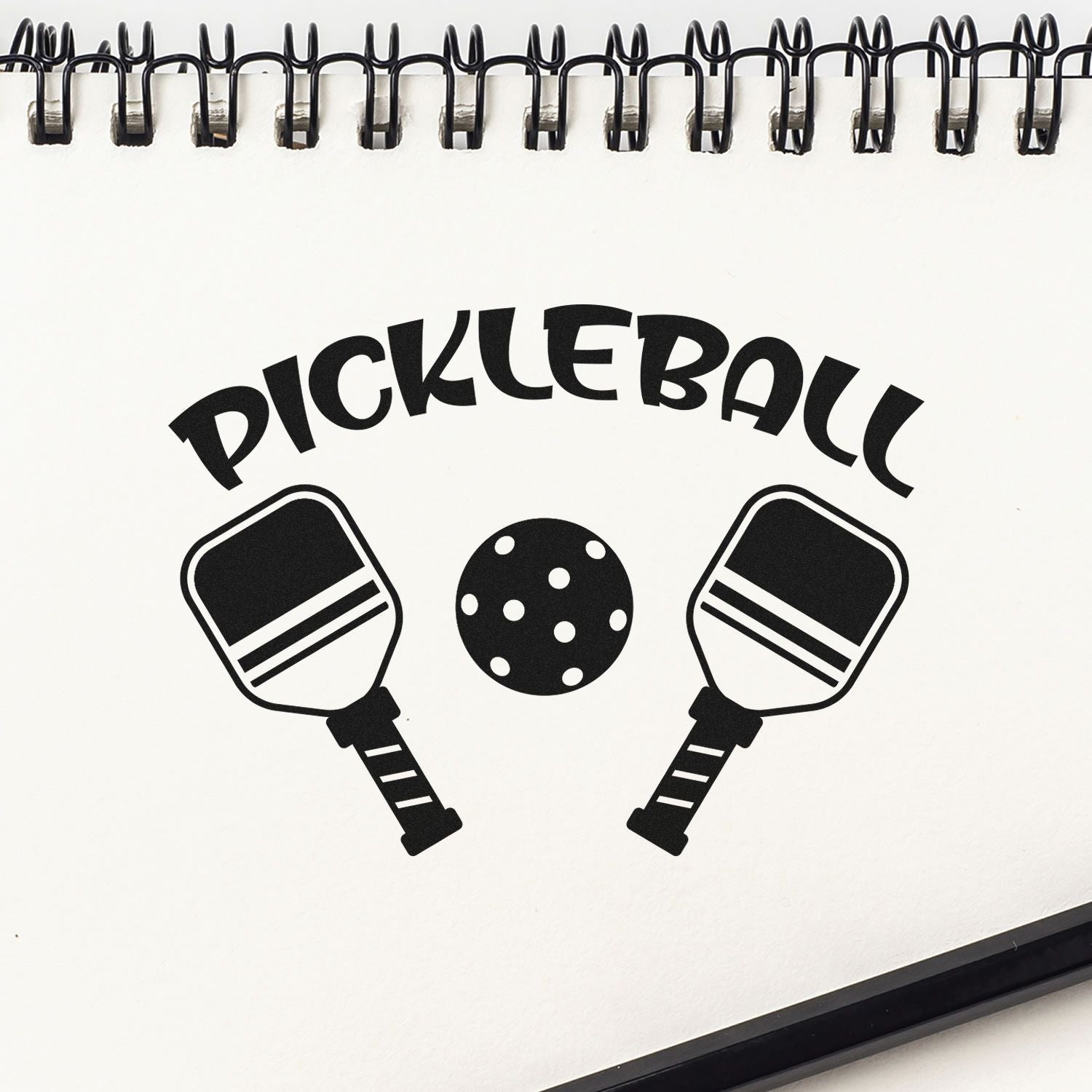 Custom pickleball rubber stamp design with paddles and ball in a spiral notebook