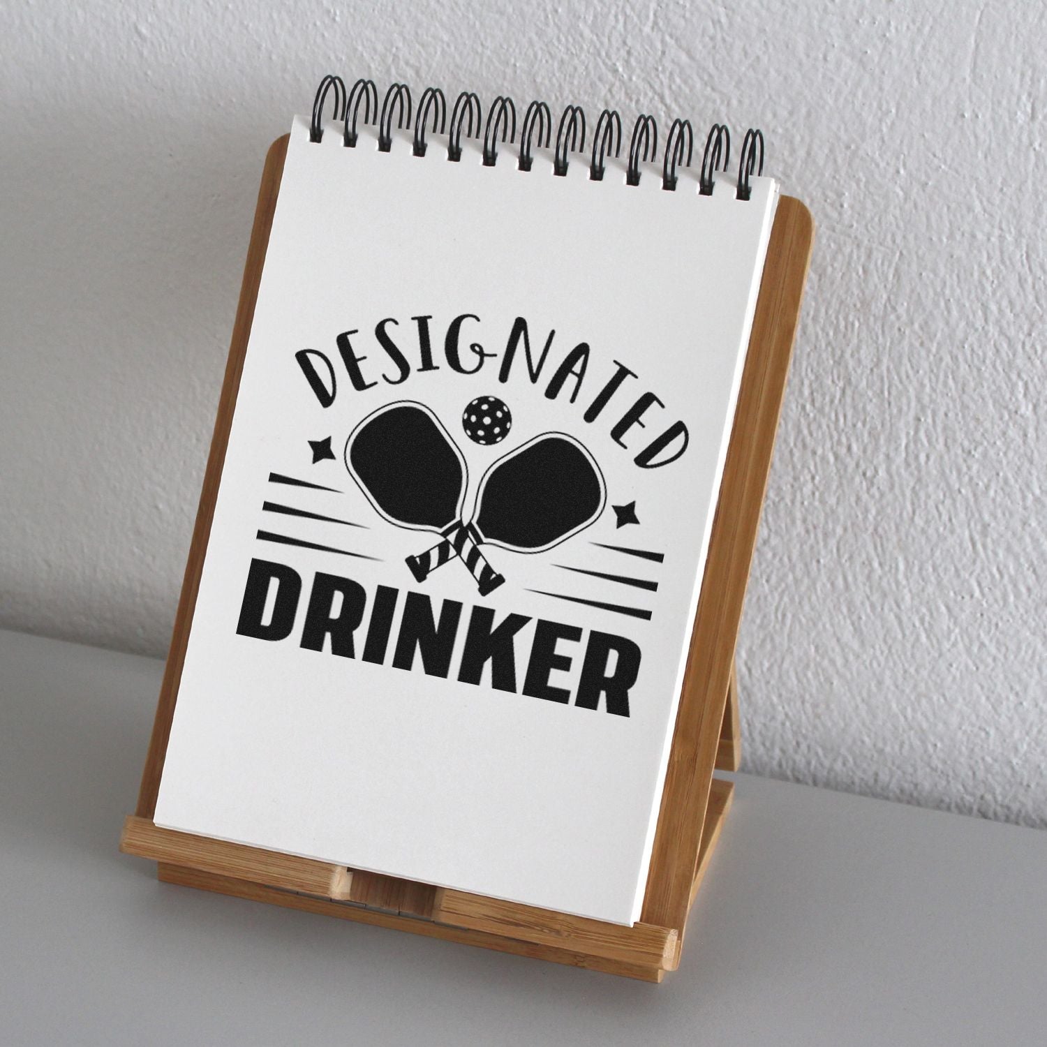 Designated Drinker rubber stamp mockup on a notebook stand with bold text and paddle graphic for party use.