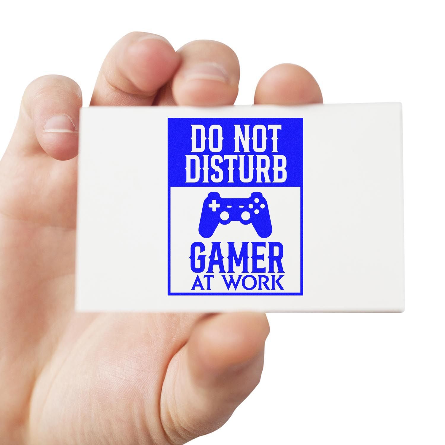 Hand holding a custom rubber stamp reading Do Not Disturb Gamer at Work with game controller icon, blue office desk design.