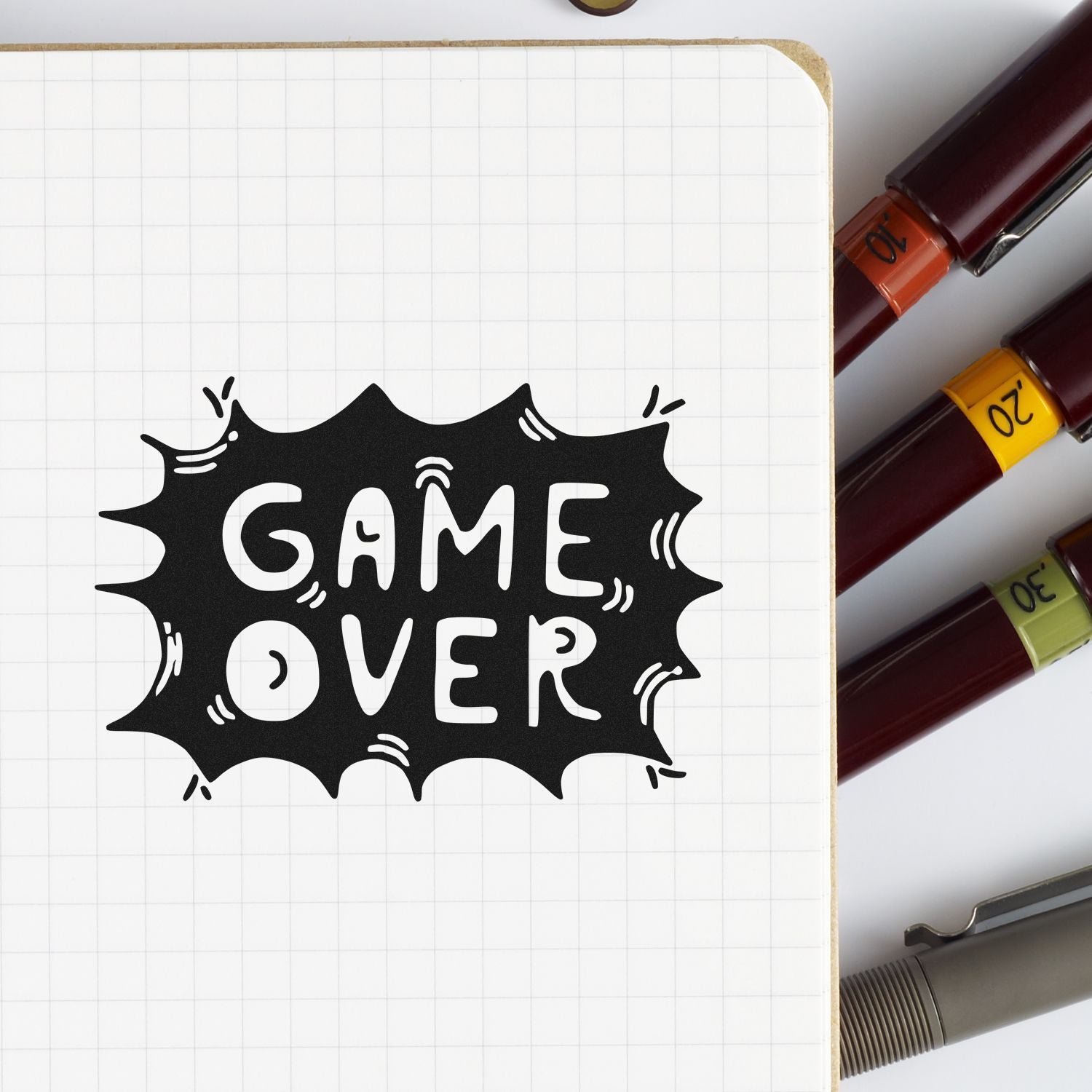 Game Over rubber stamp impression on notebook paper, shown with colored markers for journaling, planners, and craft projects.