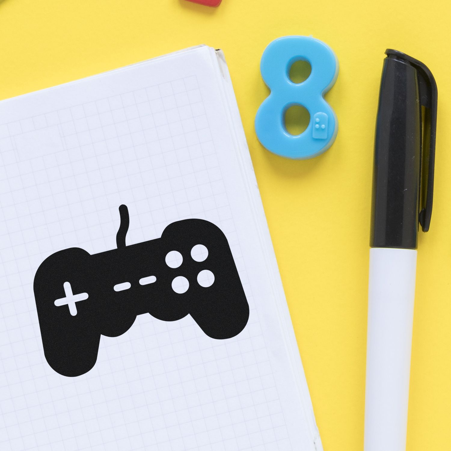 Game controller rubber stamp on notebook with number 8 stamp and marker, ideal for gaming-themed custom stationery and stamps.