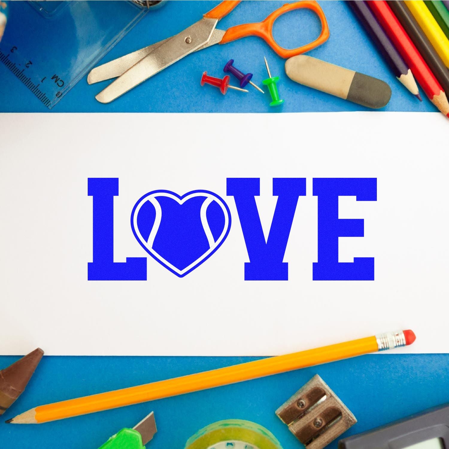 Blue LOVE heart rubber stamp impression on white paper with pencils and art supplies