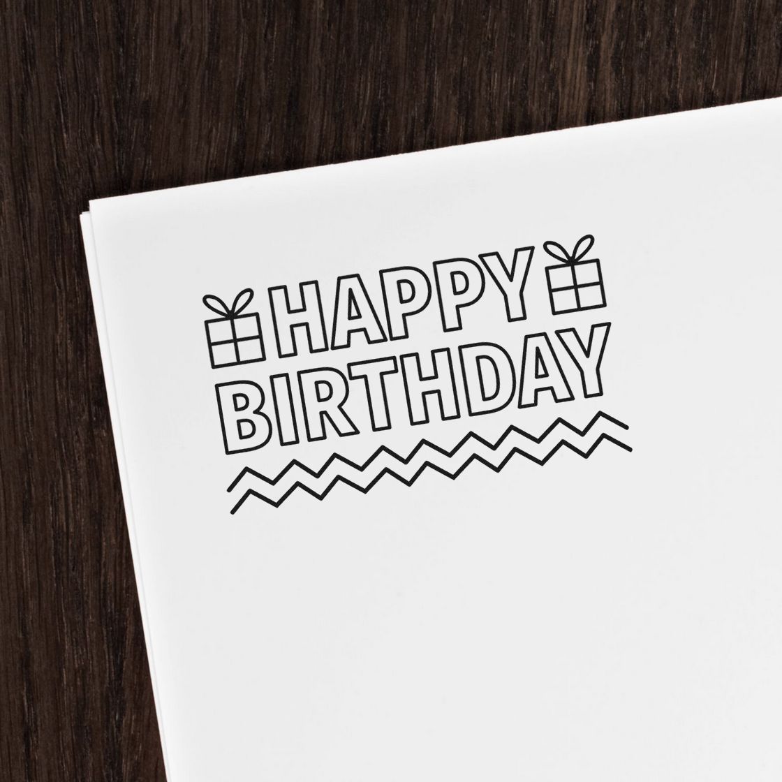Vintage Pro Happy Birthday Gifts And Zigzags Premium Wooden Stamp imprint stamped in black ink. Outlined "Happy birthday" lettering has small gifts beside HAPPY and two zigzag lines underneath.