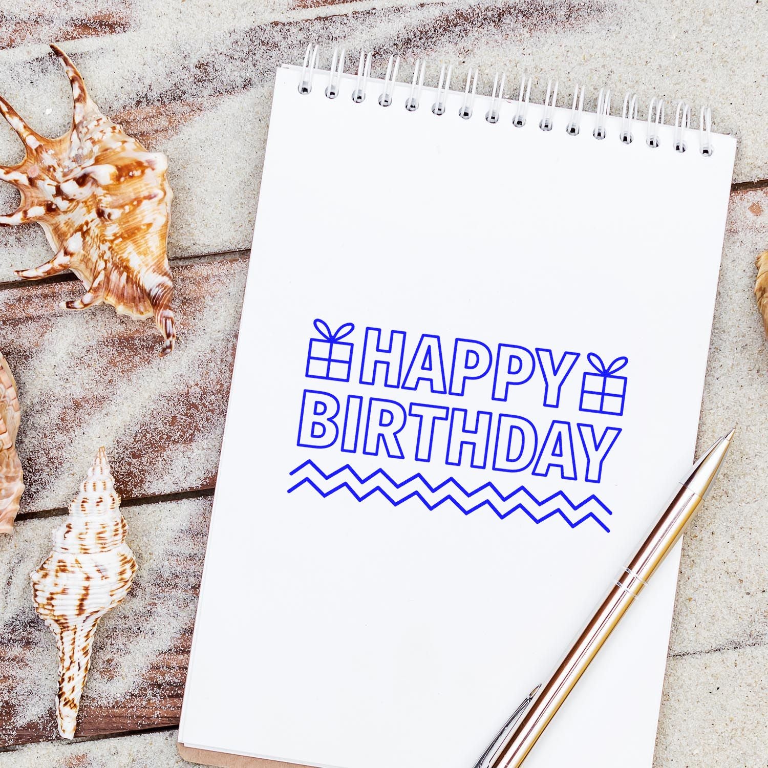 Happy birthday rubber stamp design on a spiral notebook, styled with seashells and a pen for beach-themed card making.