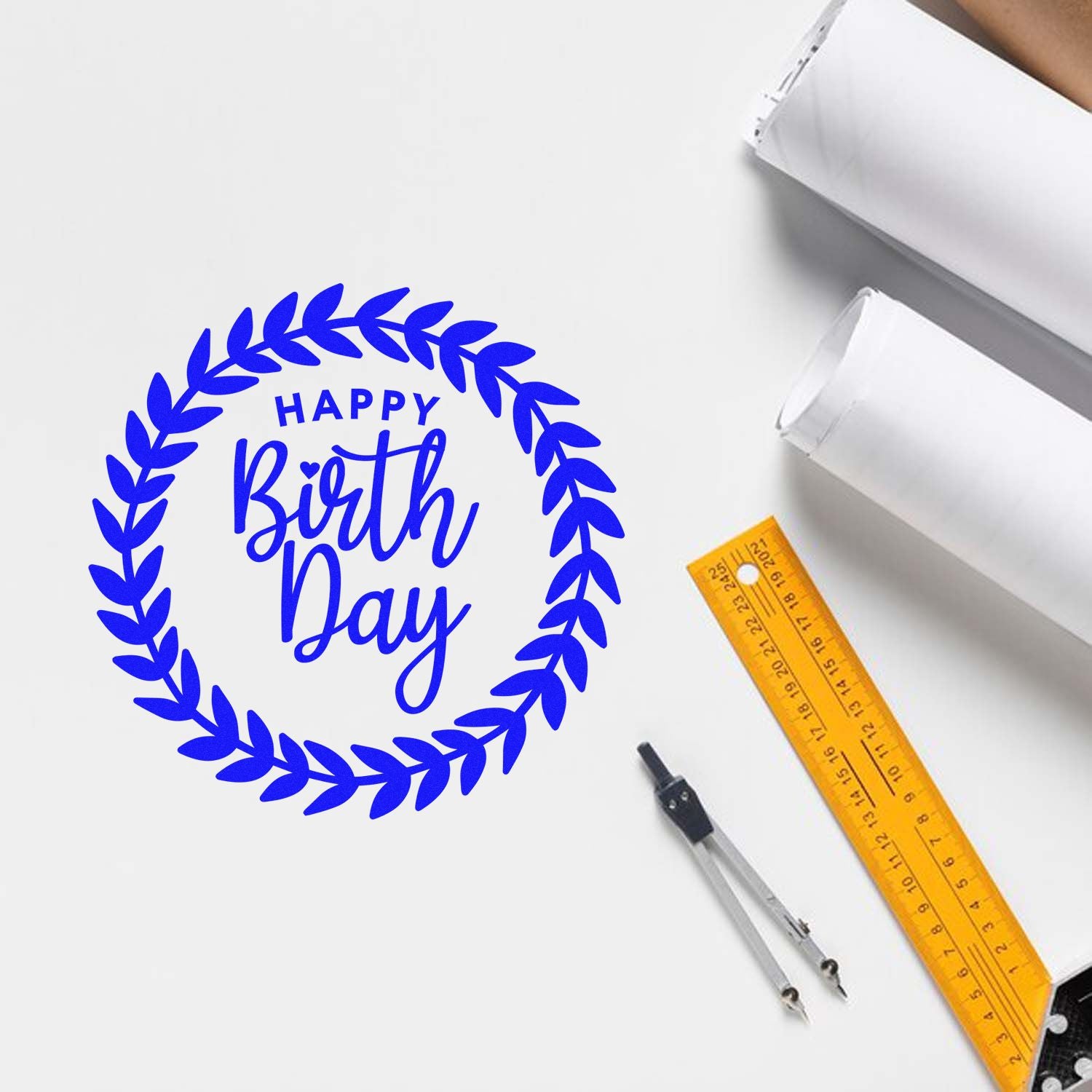 Blue Happy Birthday rubber stamp design with laurel wreath, shown on white paper for custom stationery and packaging.