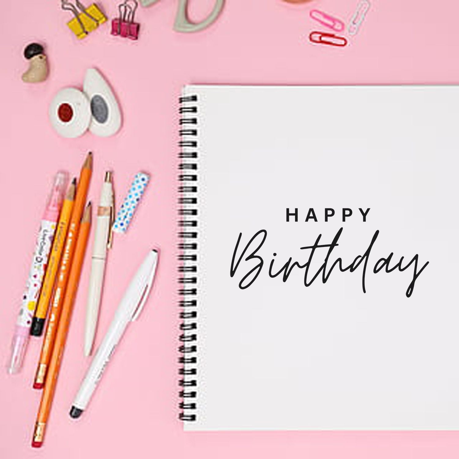 Happy Birthday rubber stamp on spiral notebook, surrounded by pens and clips, for birthday card and planner crafting