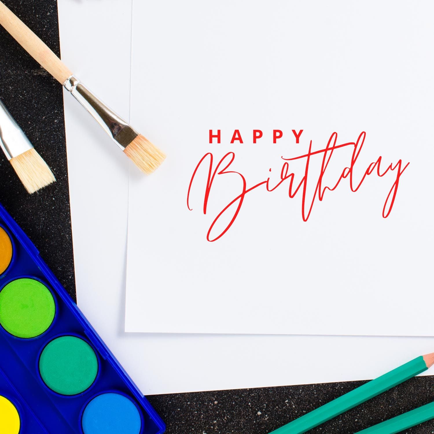 Happy Birthday rubber stamp design with watercolor paints, brushes, and pencils for handmade birthday cards.