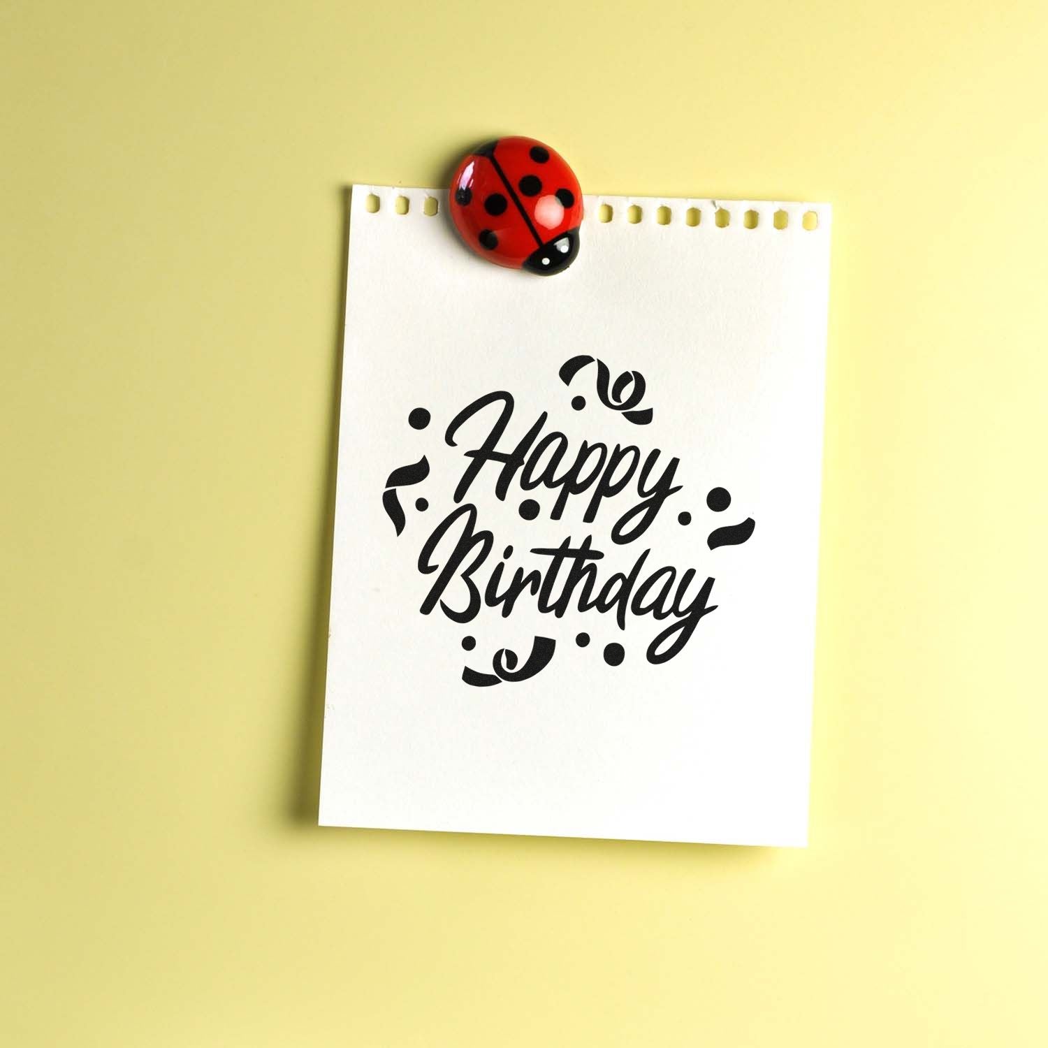 Happy Birthday rubber stamp design on white paper, clipped with a ladybug, for handmade birthday cards and crafts.
