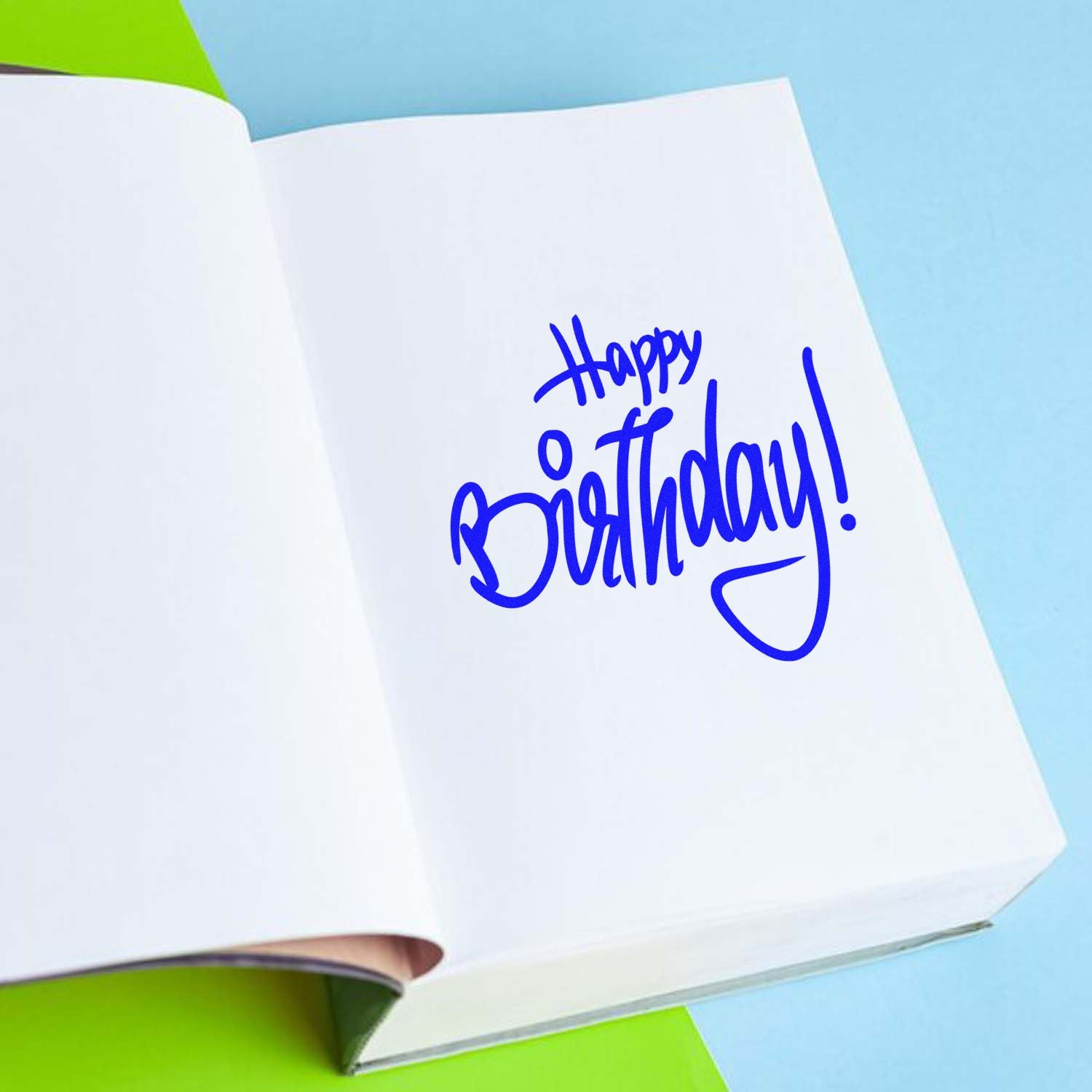 Custom birthday rubber stamp impression reading Happy Birthday! in blue ink on an open notebook page.