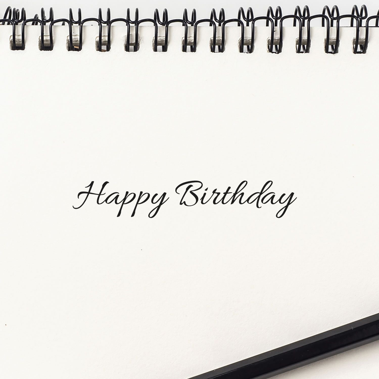 Happy Birthday rubber stamp impression in elegant script on a blank notebook page