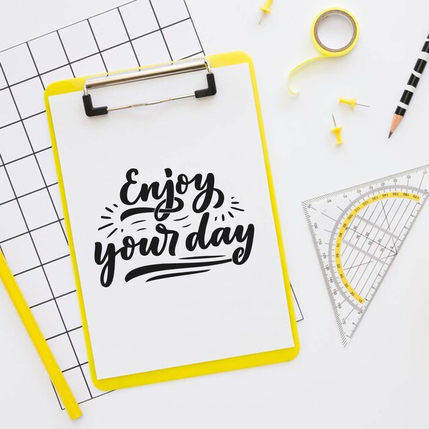 Motivational Enjoy Your Day custom rubber stamp design mockup on clipboard with stationery tools.
