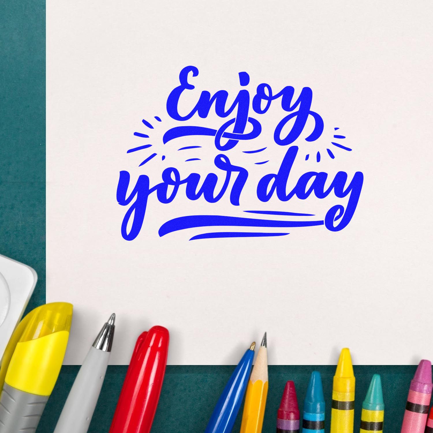Custom rubber stamp design reading Enjoy your day in blue script, shown on paper with colorful markers.