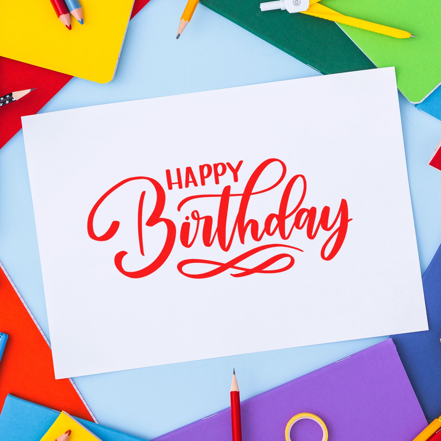 Happy Birthday rubber stamp design on blank card, surrounded by colorful stationery and pencils for party crafts.