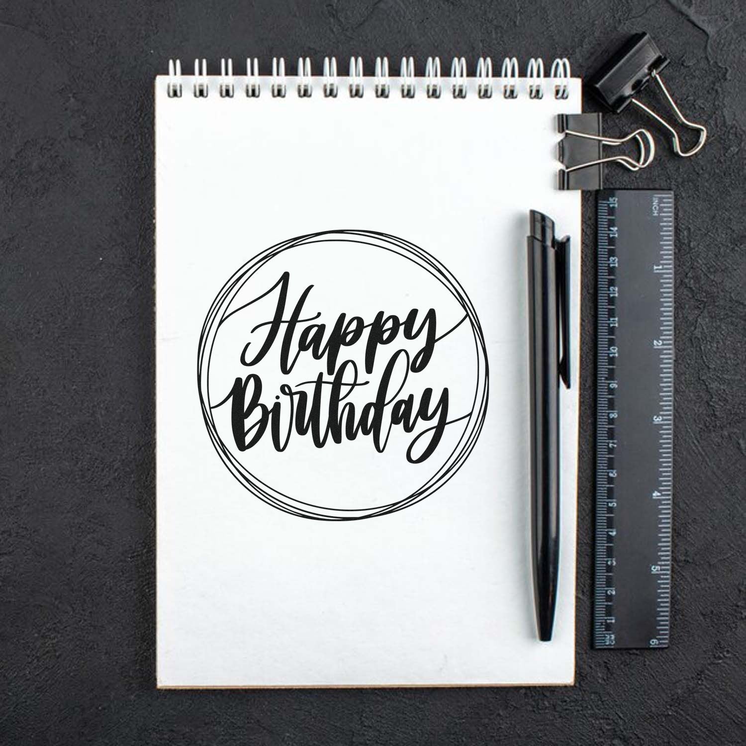 Happy Birthday rubber stamp mockup on a notebook with pen and ruler, ideal for custom birthday craft designs.