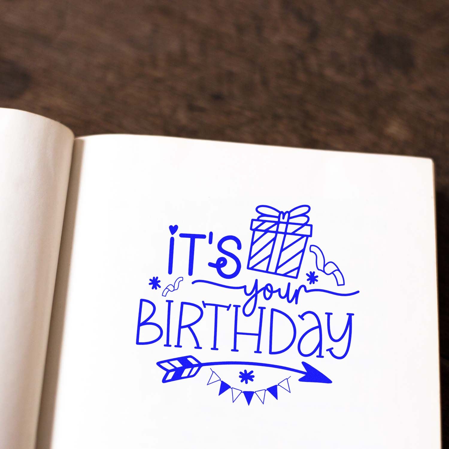 Custom birthday rubber stamp design with gift, arrow, and bunting on a notebook page.
